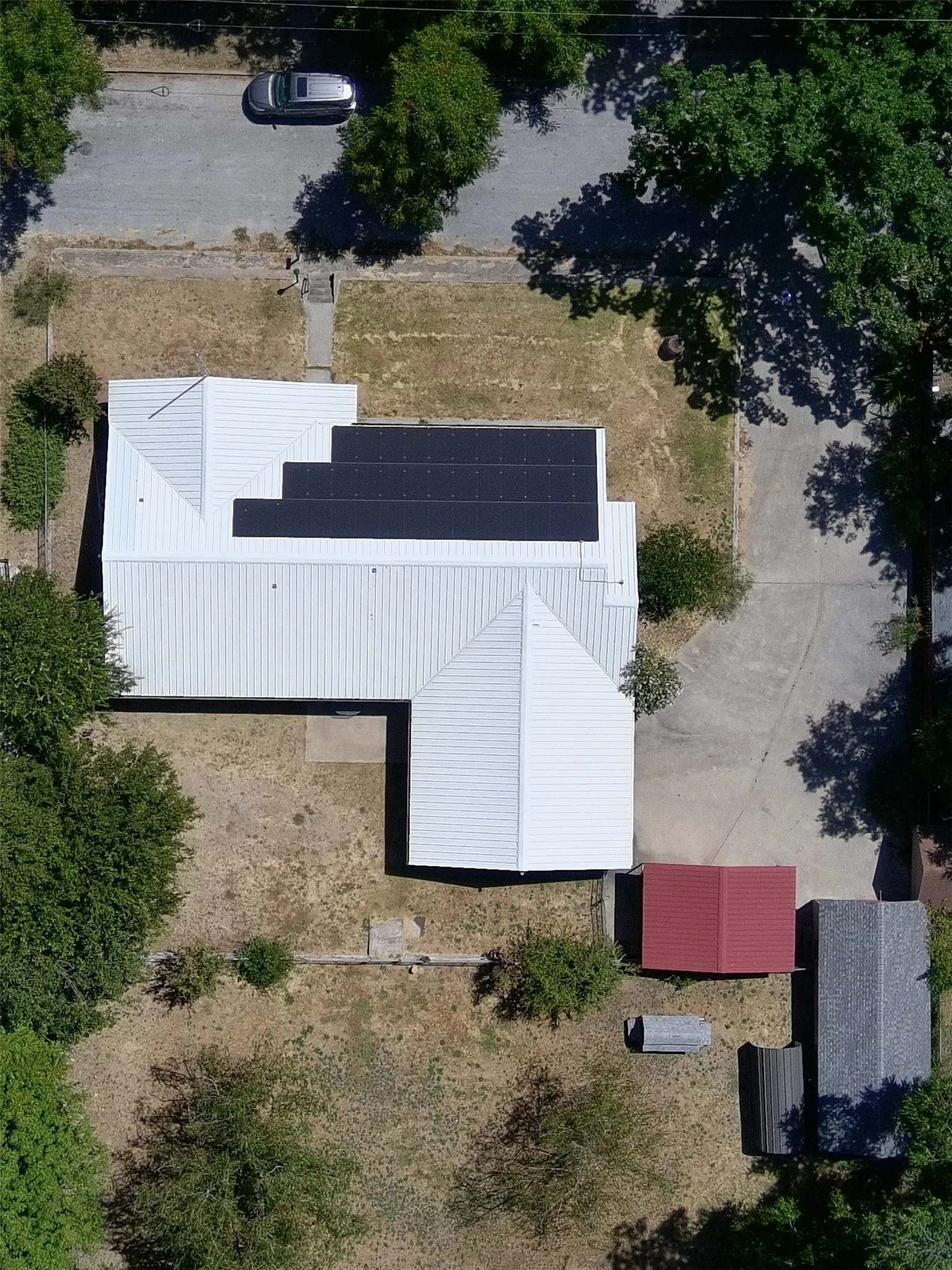 Metal roof with integrated solar panels, concrete driveway, and additional outbuildings