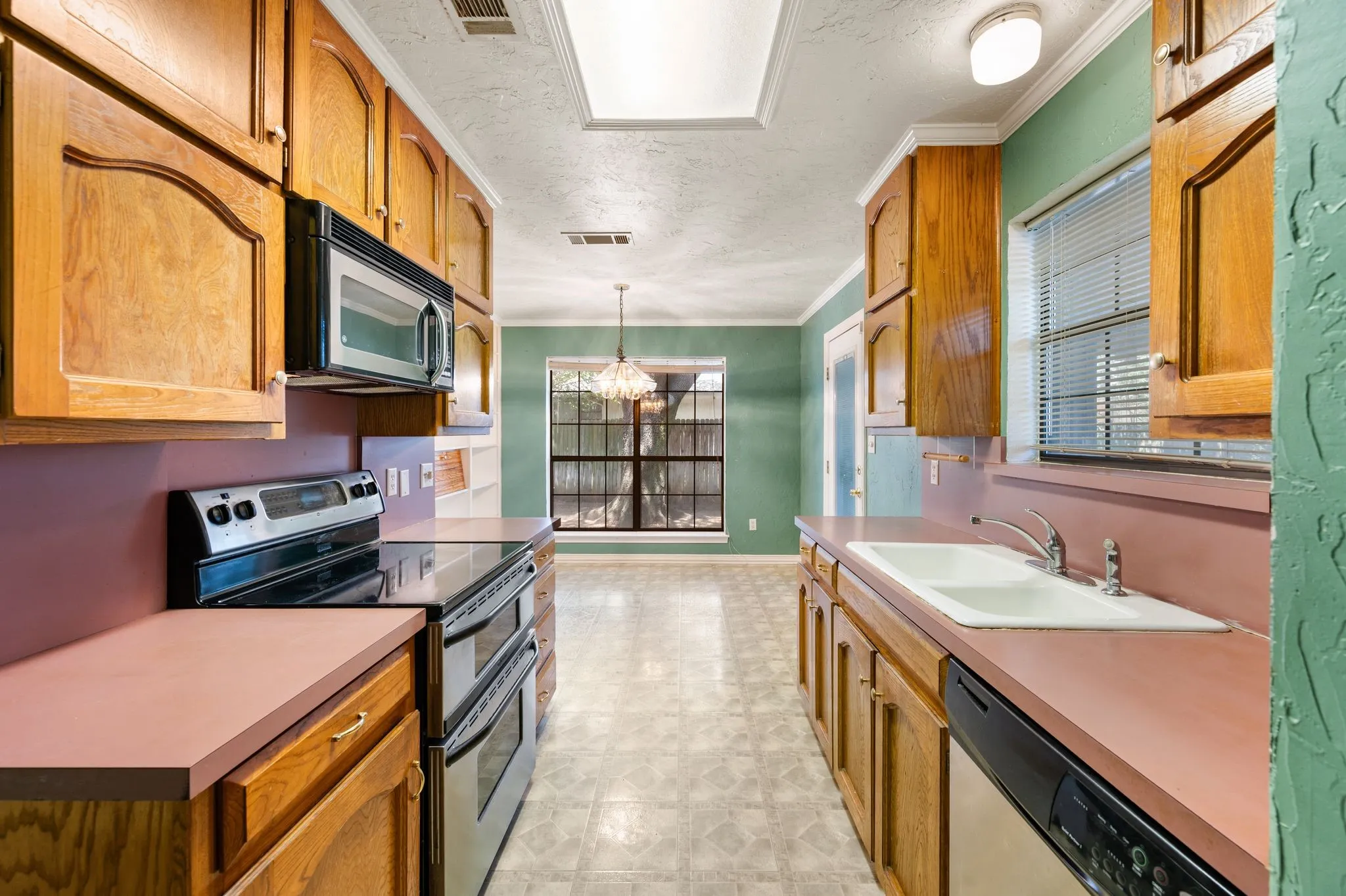 Galley kitchen featuring wood cabinetry, stainless steel appliances, and a double basin sink