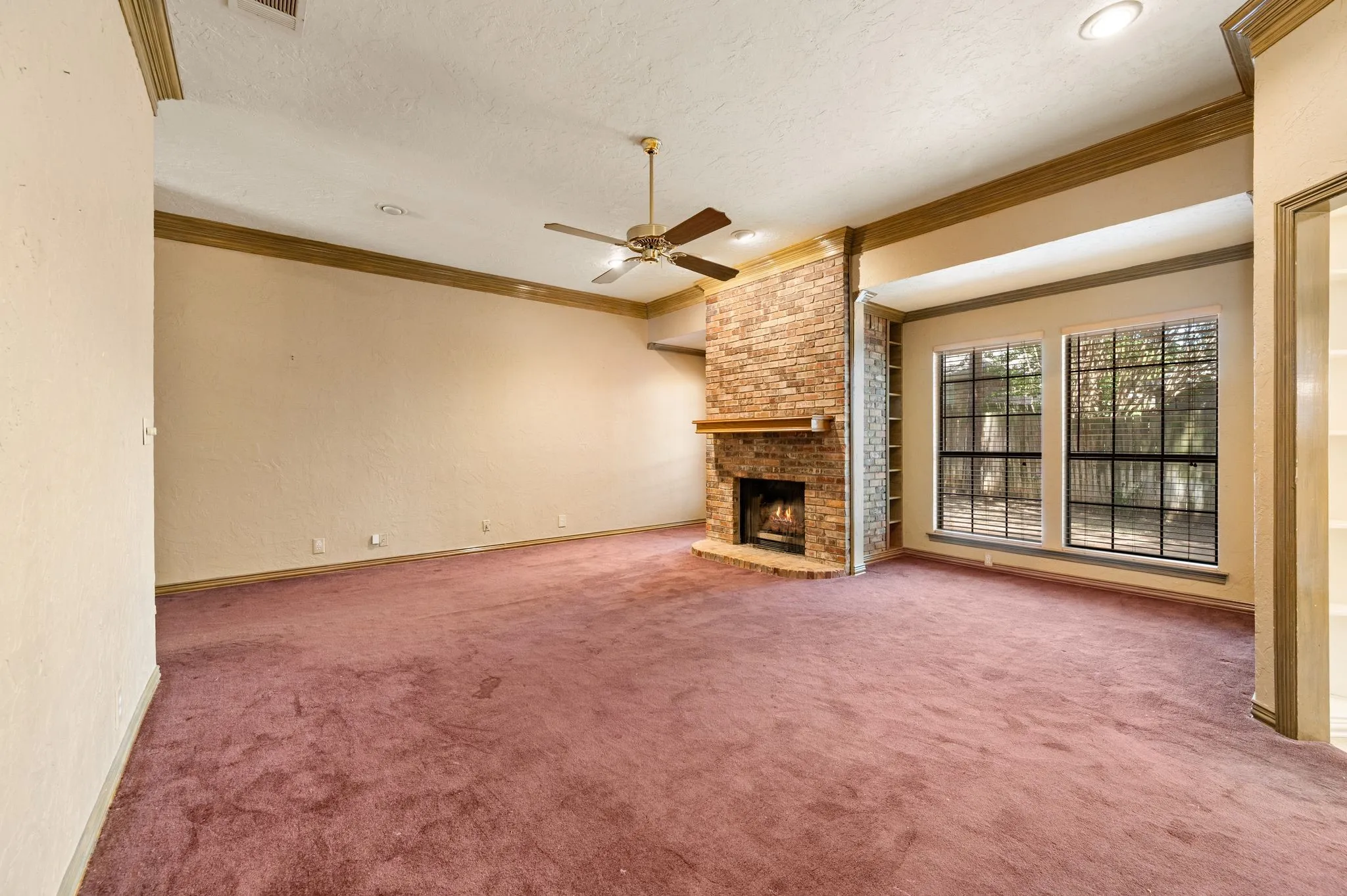 Spacious room featuring a brick-clad fireplace with a wood mantle, two large windows, recessed lighting, and a ceiling fan