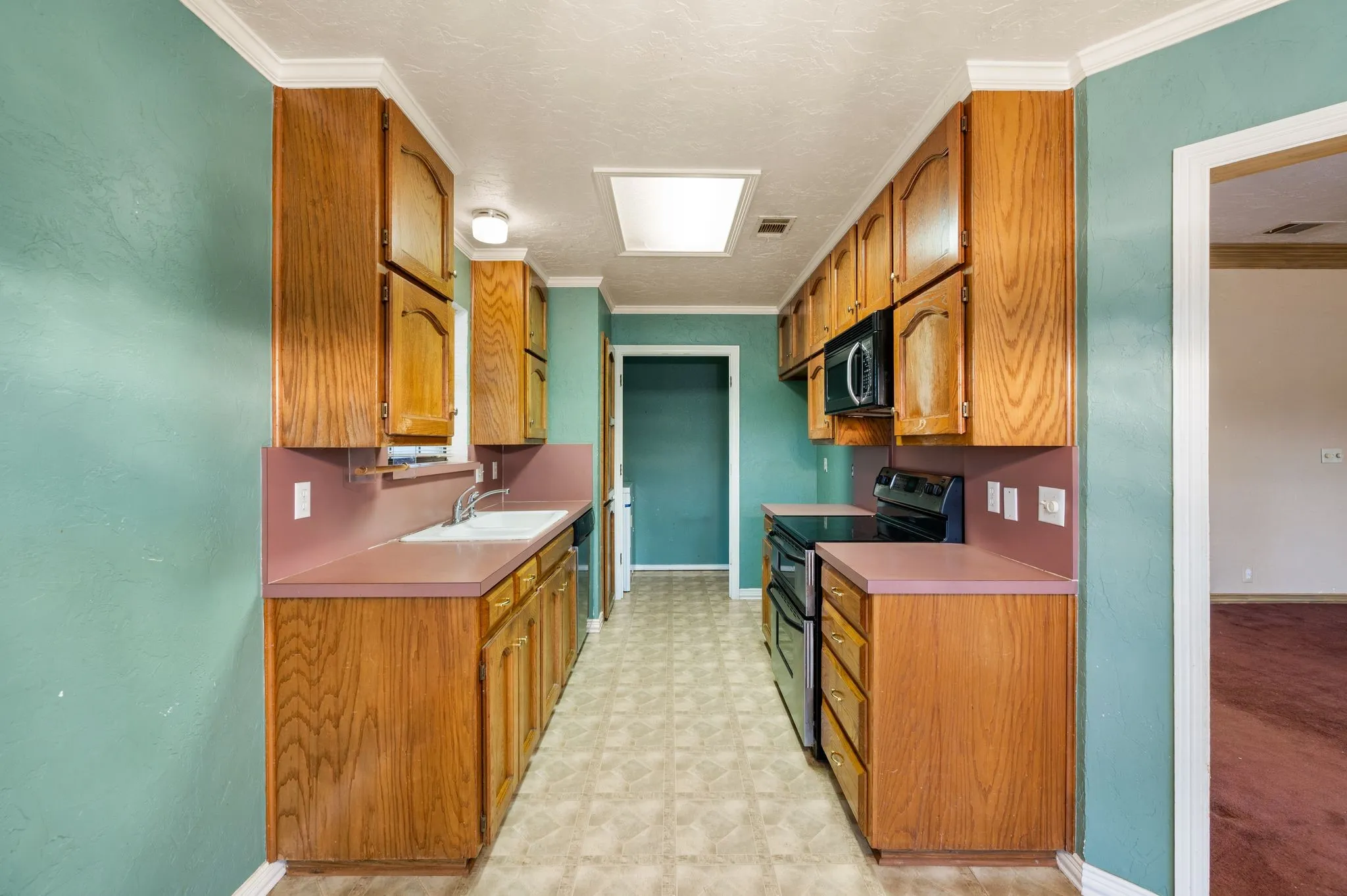 Galley kitchen featuring wood-finish cabinetry, solid surface countertops, a built-in microwave, and an electric range