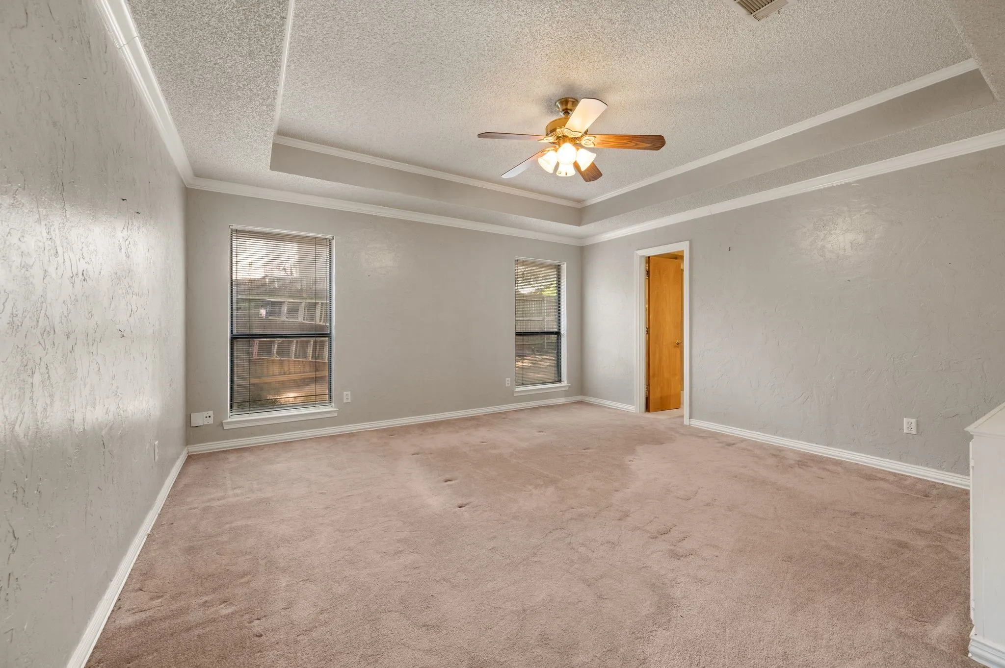 Tray ceiling with crown molding, ceiling fan, and carpeted flooring