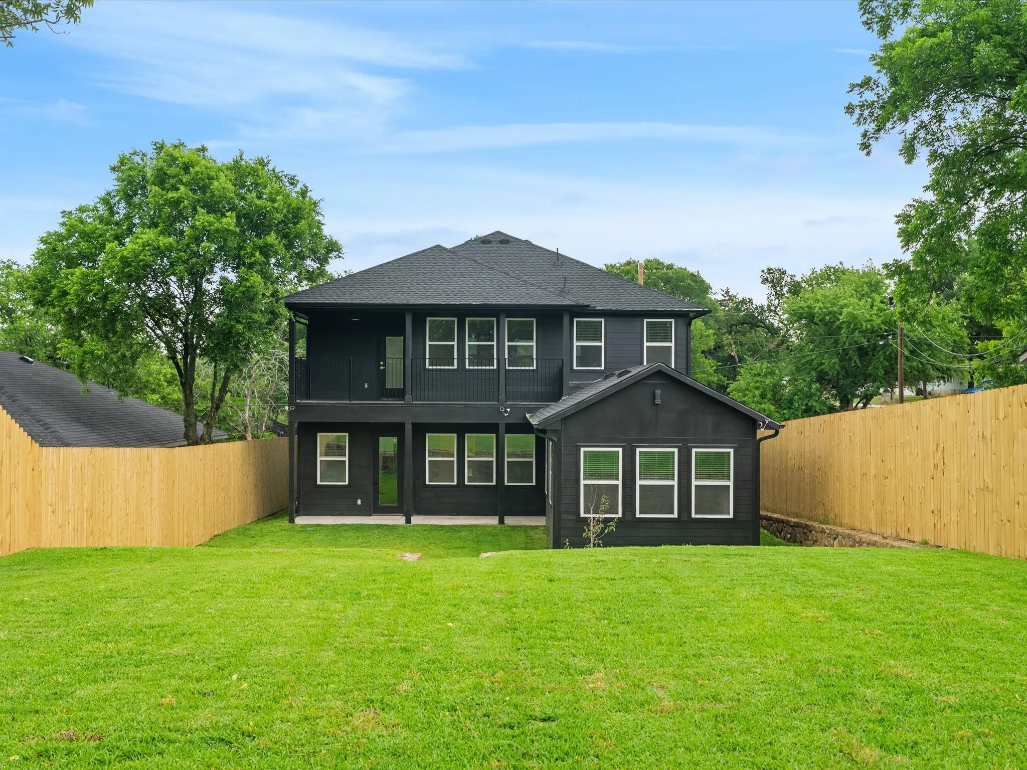 Expansive backyard with a manicured lawn, full privacy fencing, and a two-story exterior with a covered balcony