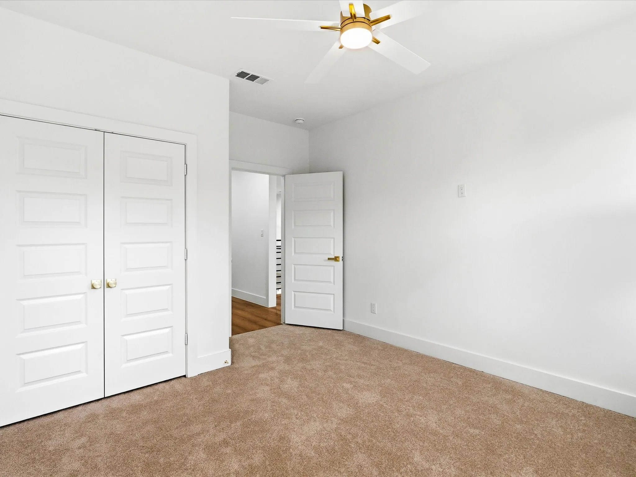 Neutral wall paint with carpeted flooring, a ceiling fan with integrated lighting, and a paneled closet with brass hardware