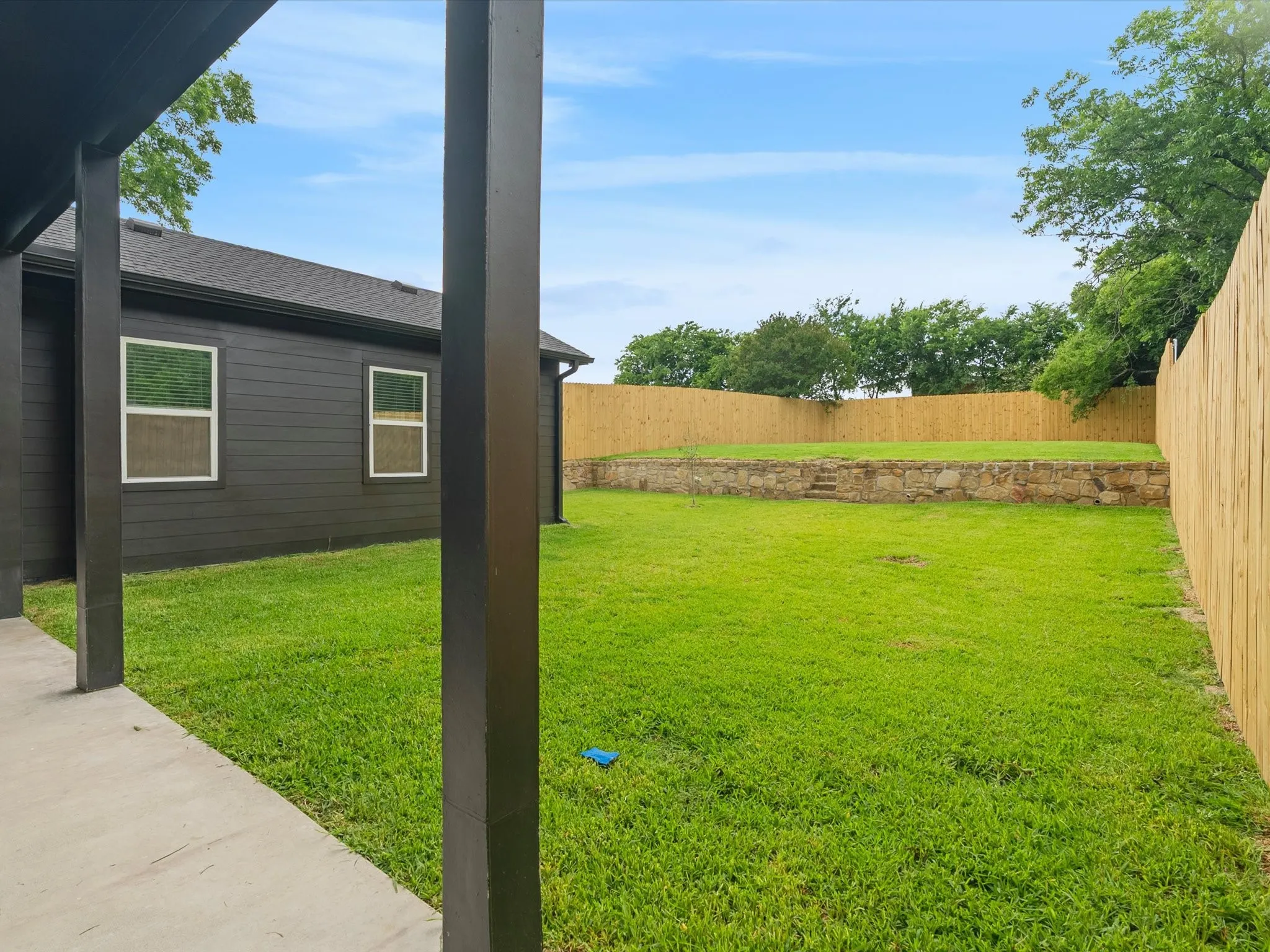 Expansive backyard featuring a manicured lawn, full privacy fencing, and a stone retaining wall