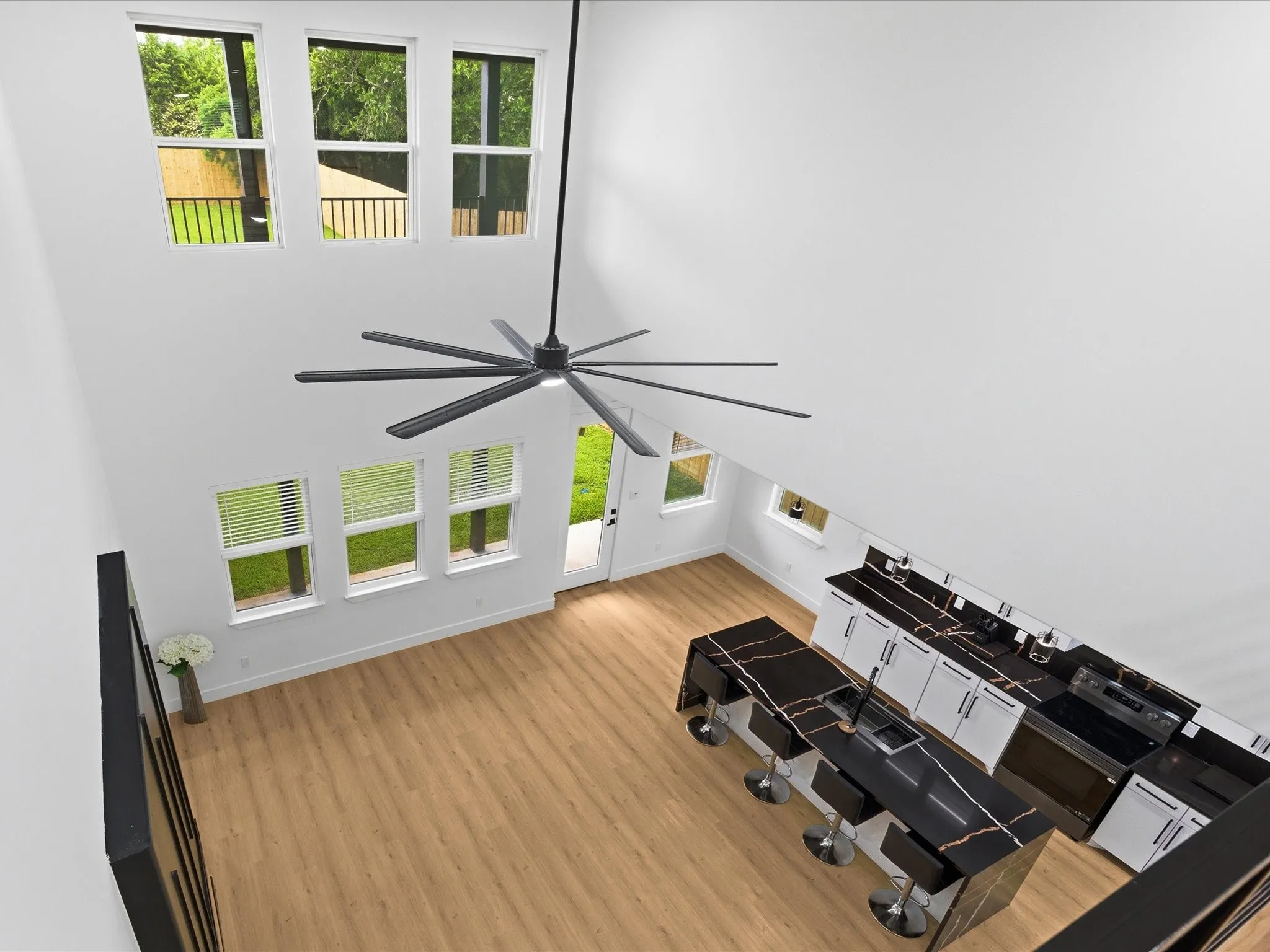 High ceilings with an expansive ceiling fan, multiple large windows, wood-finish flooring, a kitchen island with seating, and white cabinetry with dark countertops