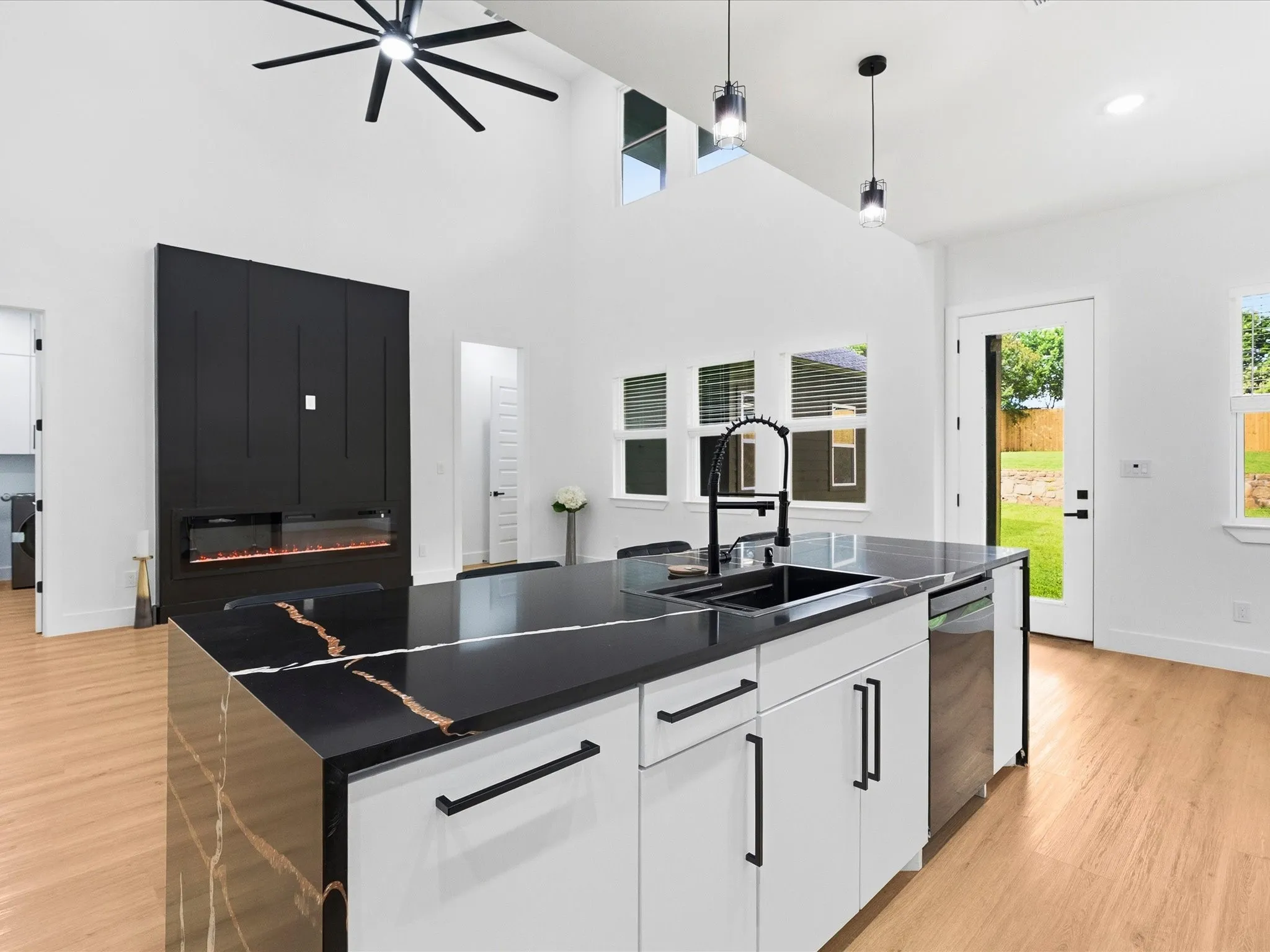 Vaulted ceiling with an overhead fan, wood-finish flooring, built-in fireplace, kitchen island with integrated sink, and pendant lighting