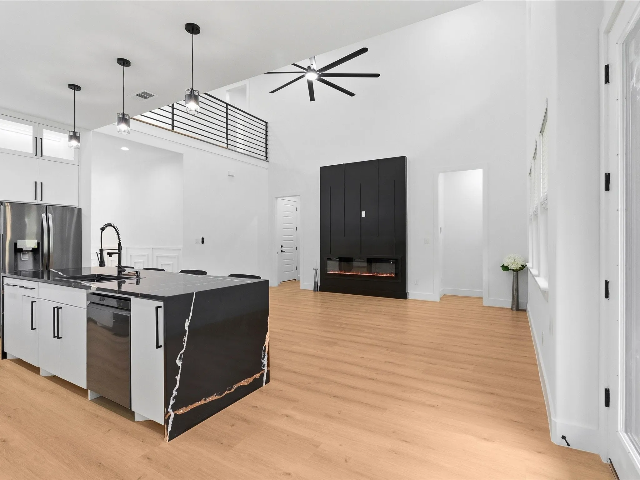 Open-concept living area featuring high vaulted ceilings, wood-finish flooring, a contemporary fireplace, a kitchen island with stone countertops, and a modern ceiling fan