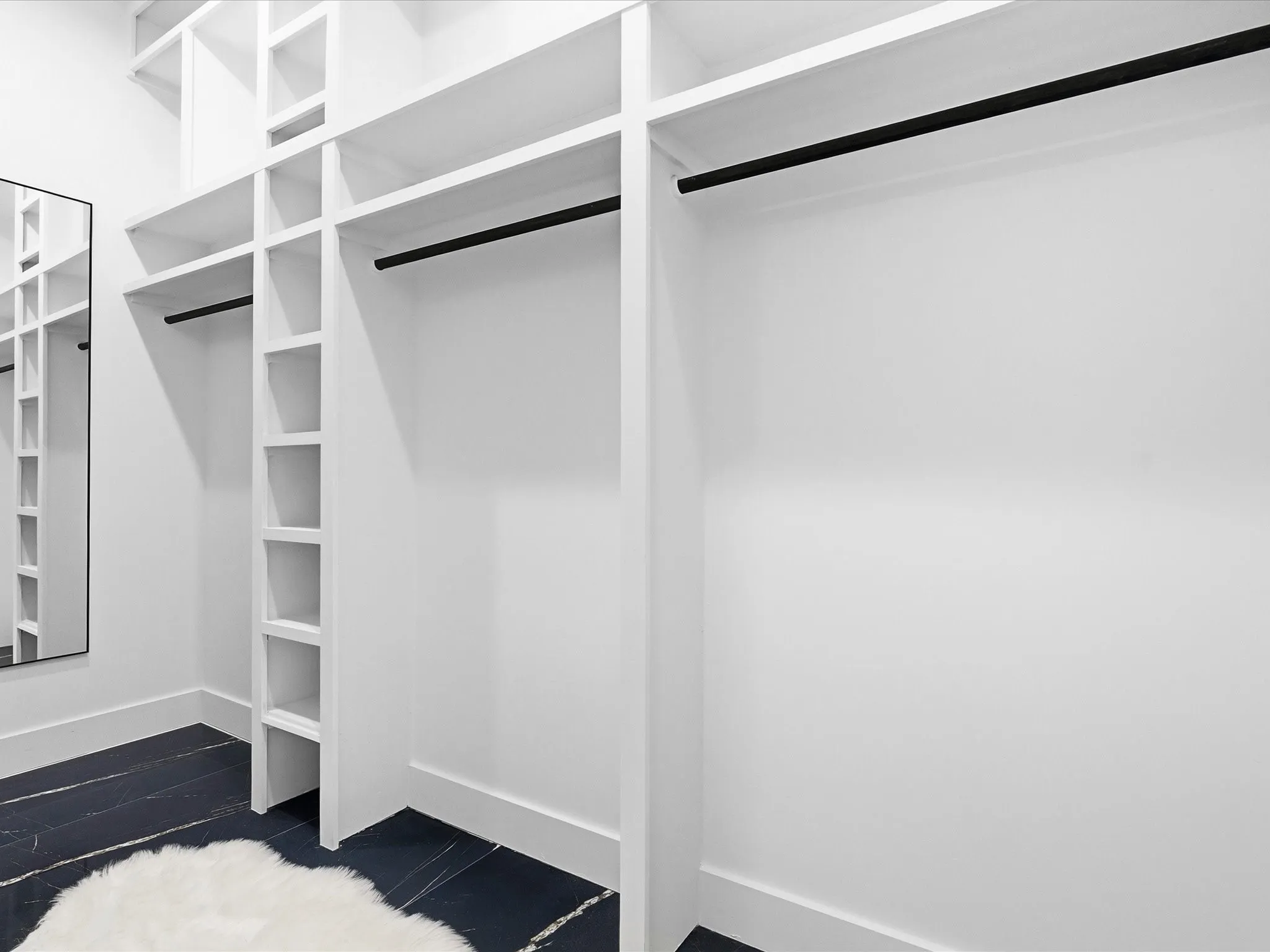 Built-in closet system featuring white shelving, multiple hanging rods, and dark-toned flooring