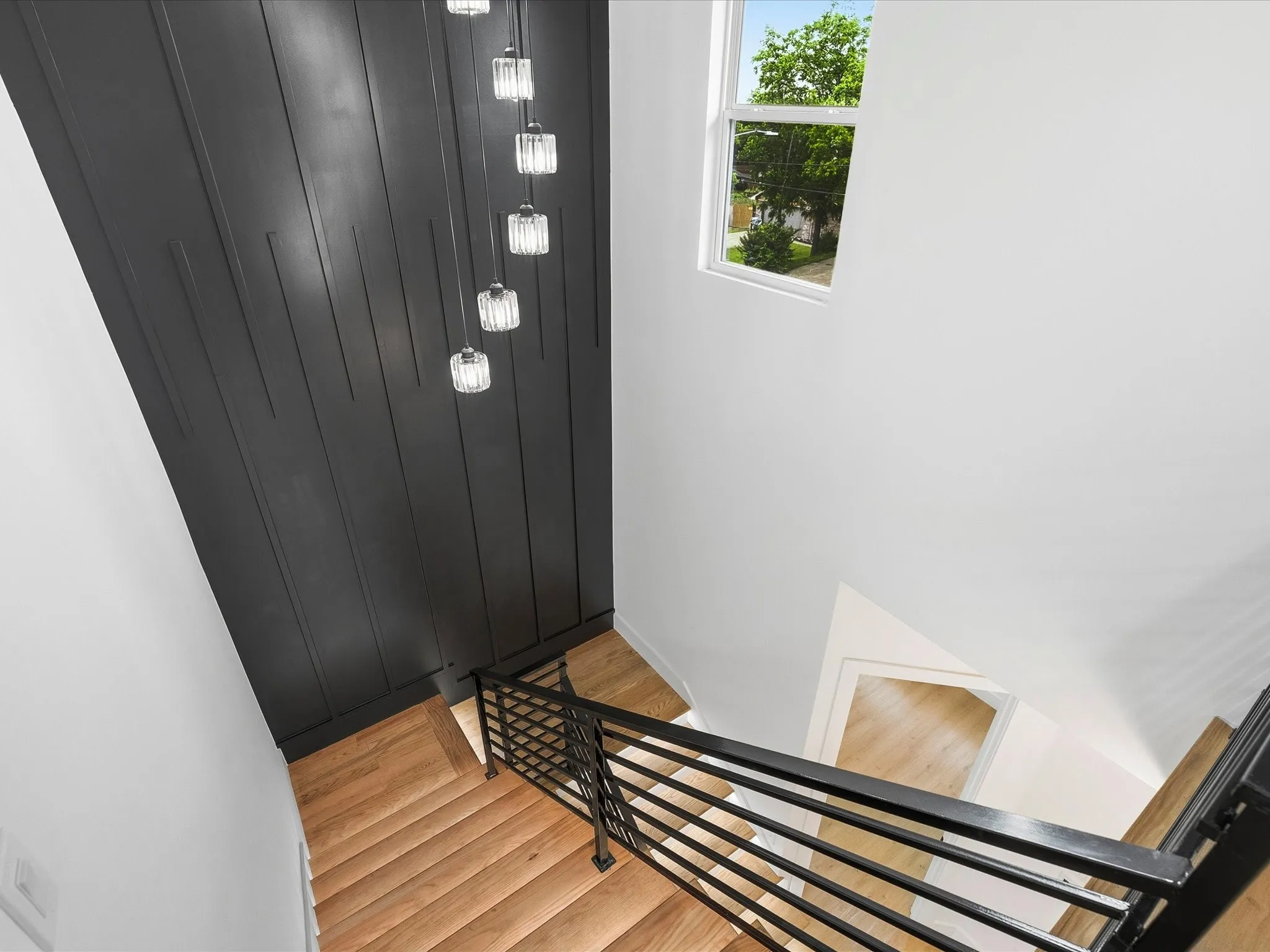Wood-finish staircase with black metal railing, a prominent dark accent wall, suspended crystal light fixtures, and a clear window