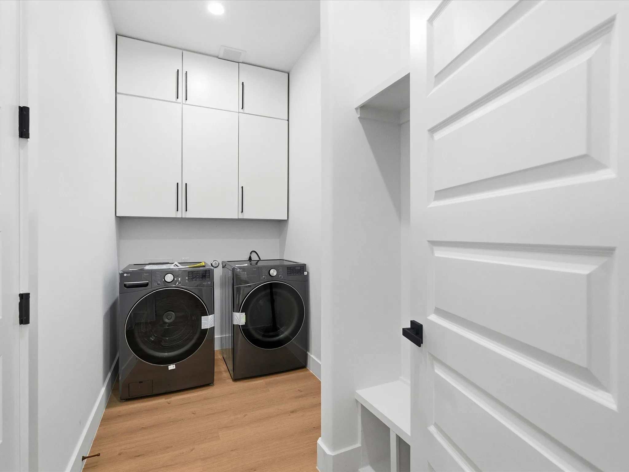 Built-in white cabinetry with matte black hardware, wood-finish flooring, and a white paneled door