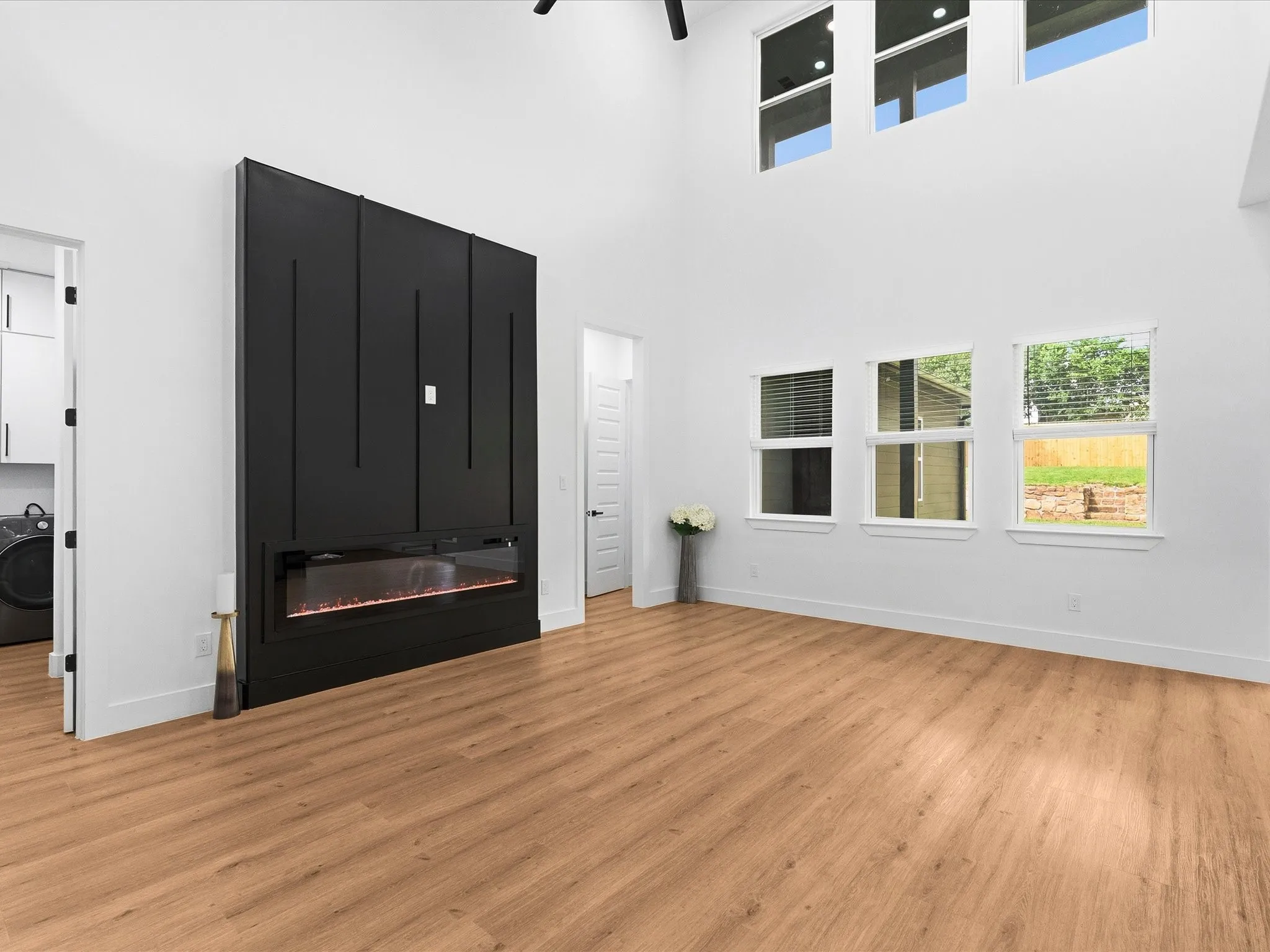 Vaulted ceilings with high transom windows, wood-finish flooring, and a contemporary black accent wall featuring an electric fireplace