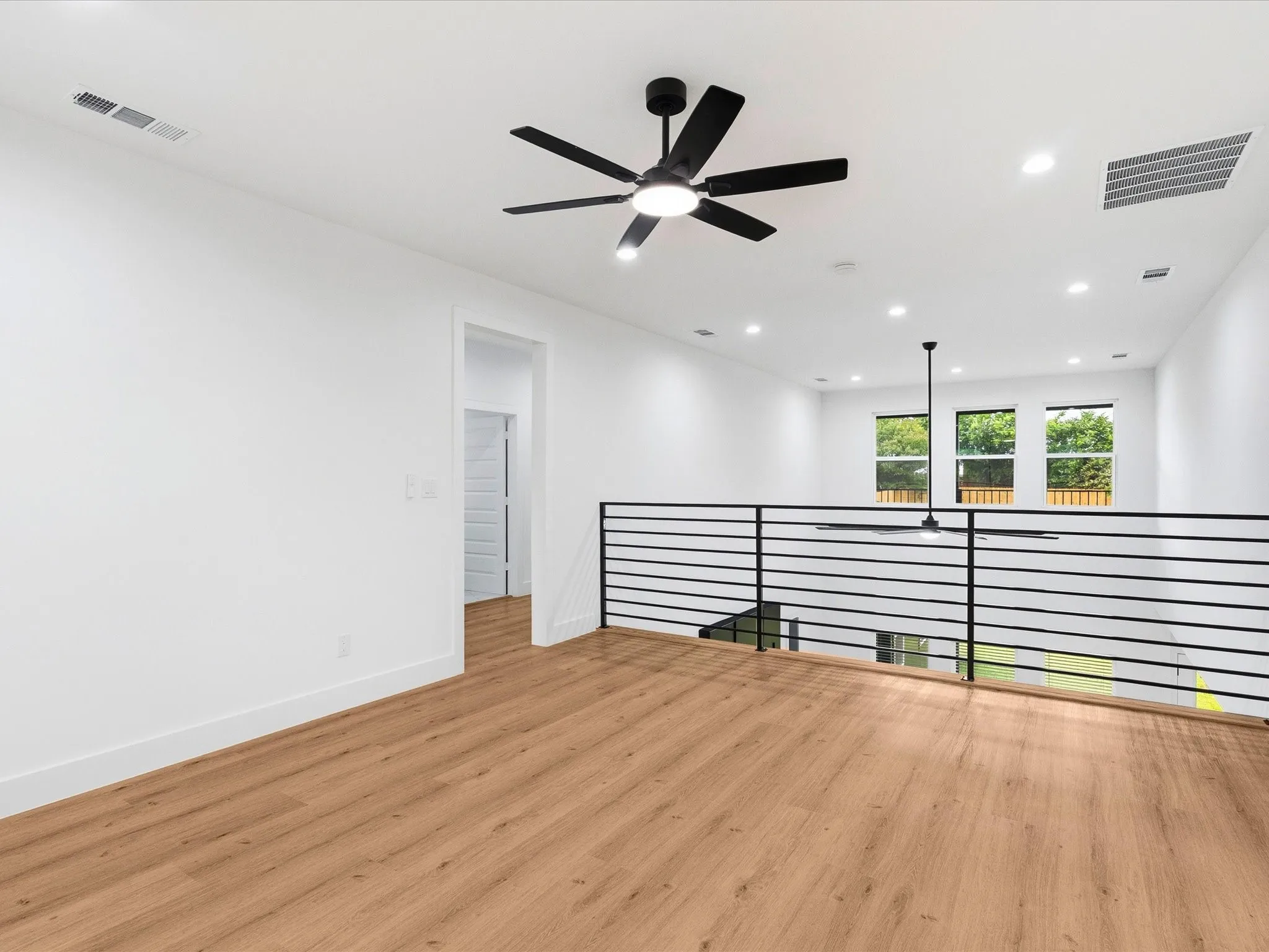 Loft space featuring wood-finish flooring, a modern black ceiling fan, recessed lighting, and a contemporary black horizontal railing
