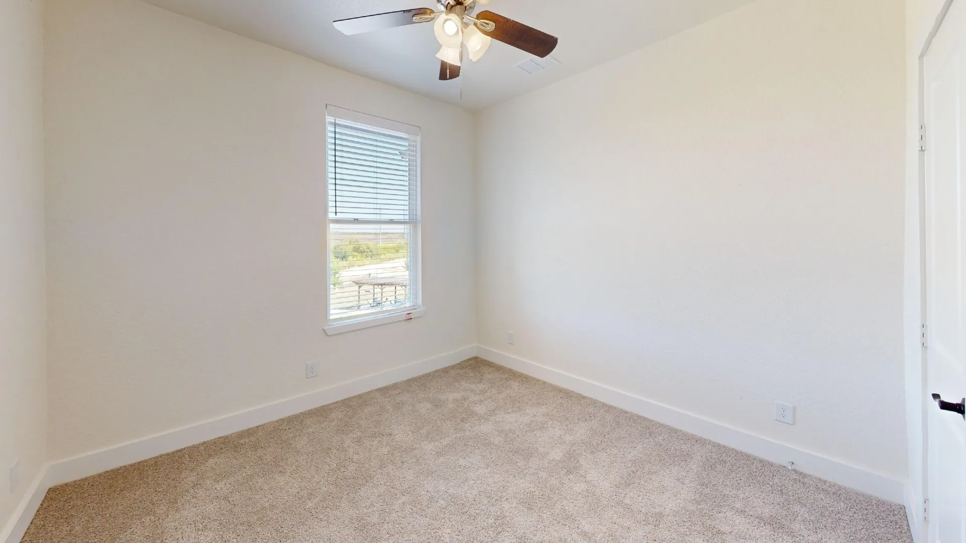 Neutral wall paint, textured carpet flooring, window with blinds, ceiling fan with integrated lighting, and a paneled interior door