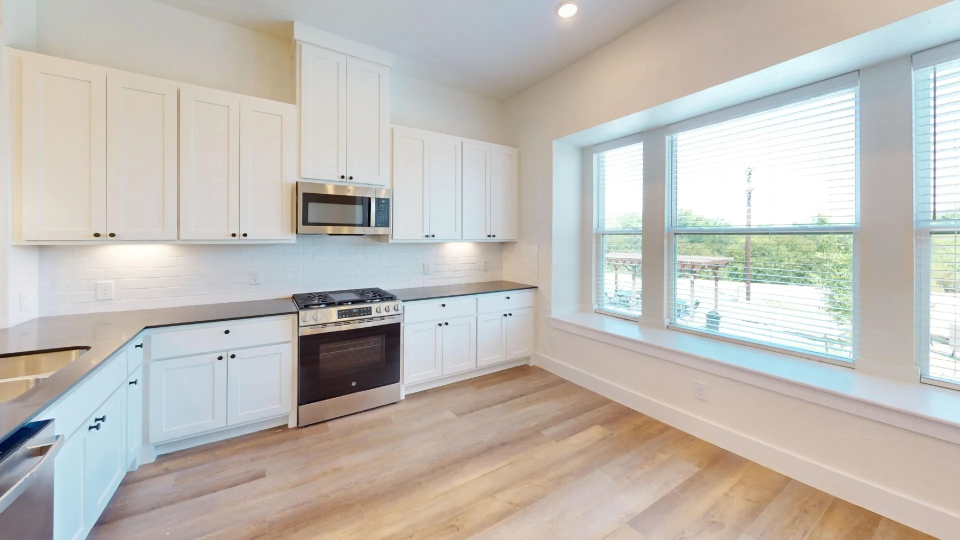 Kitchen featuring white cabinetry, stainless steel appliances, wood-finish flooring, a subway tile backsplash, and extensive window space
