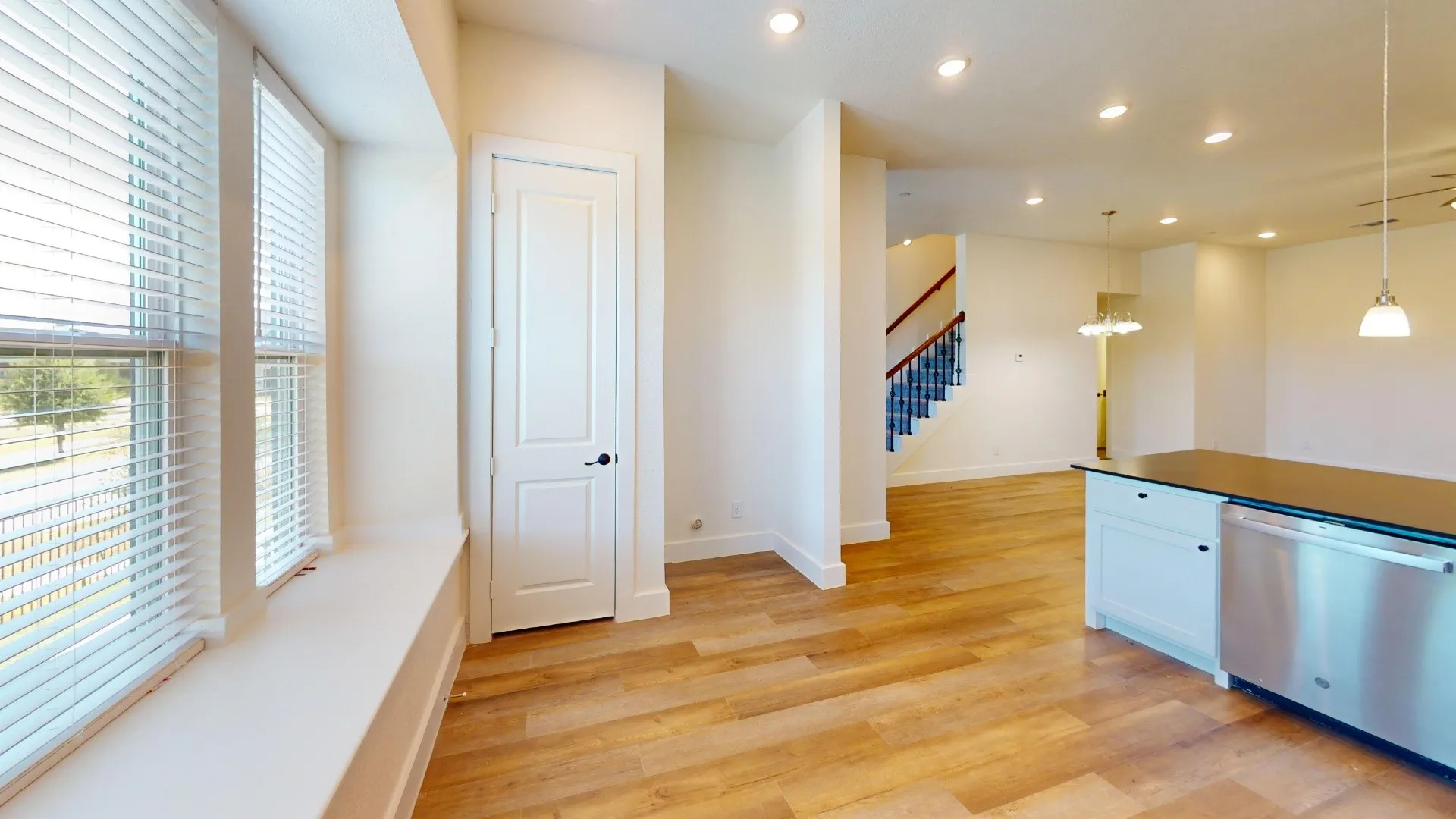 Wood-finish flooring throughout, stainless steel dishwasher, white recessed panel cabinetry, dark countertop, and recessed lighting