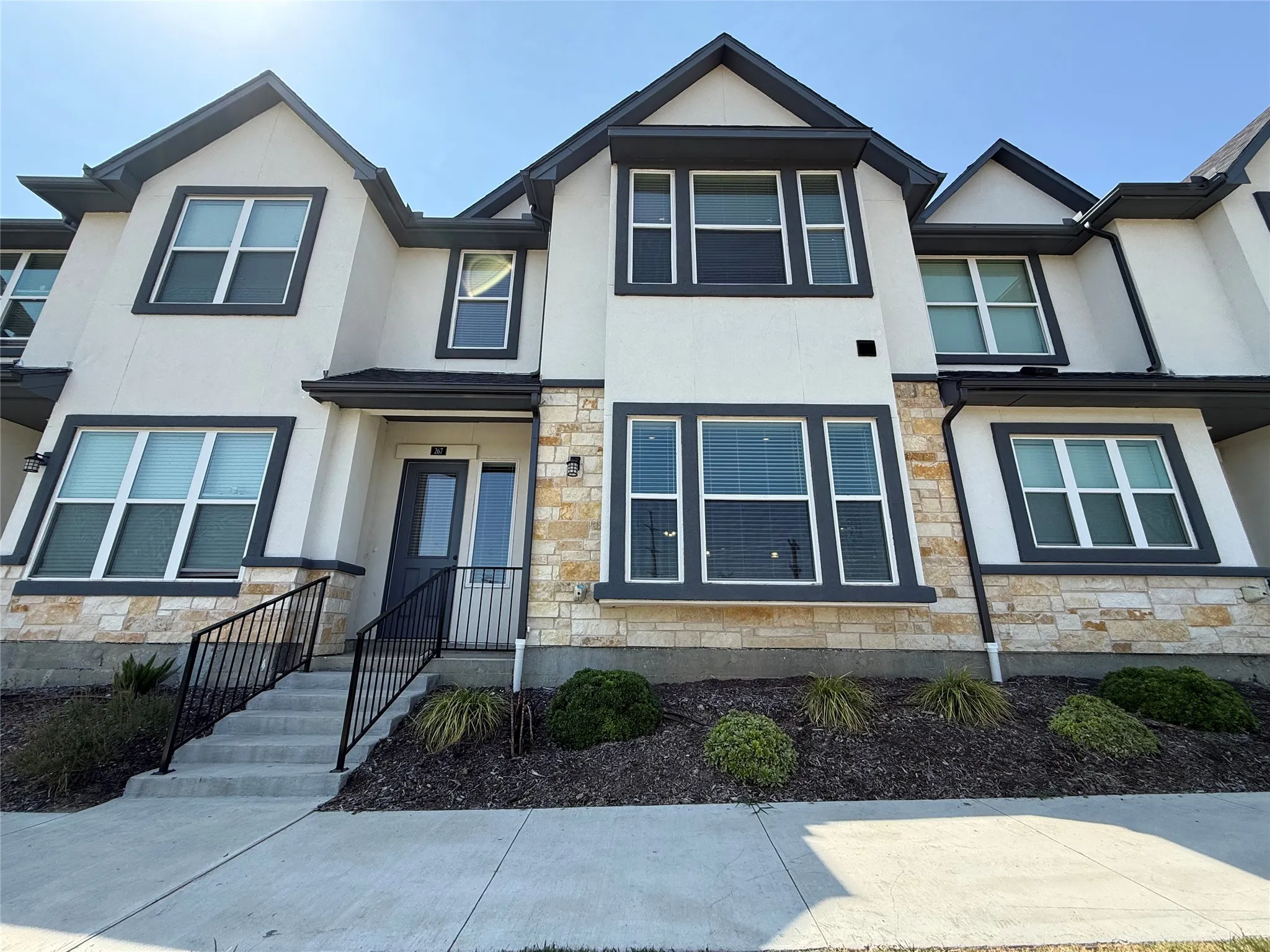 Modern facade with a combination of stucco and stone veneer, dark trim windows, and a dark entry door
