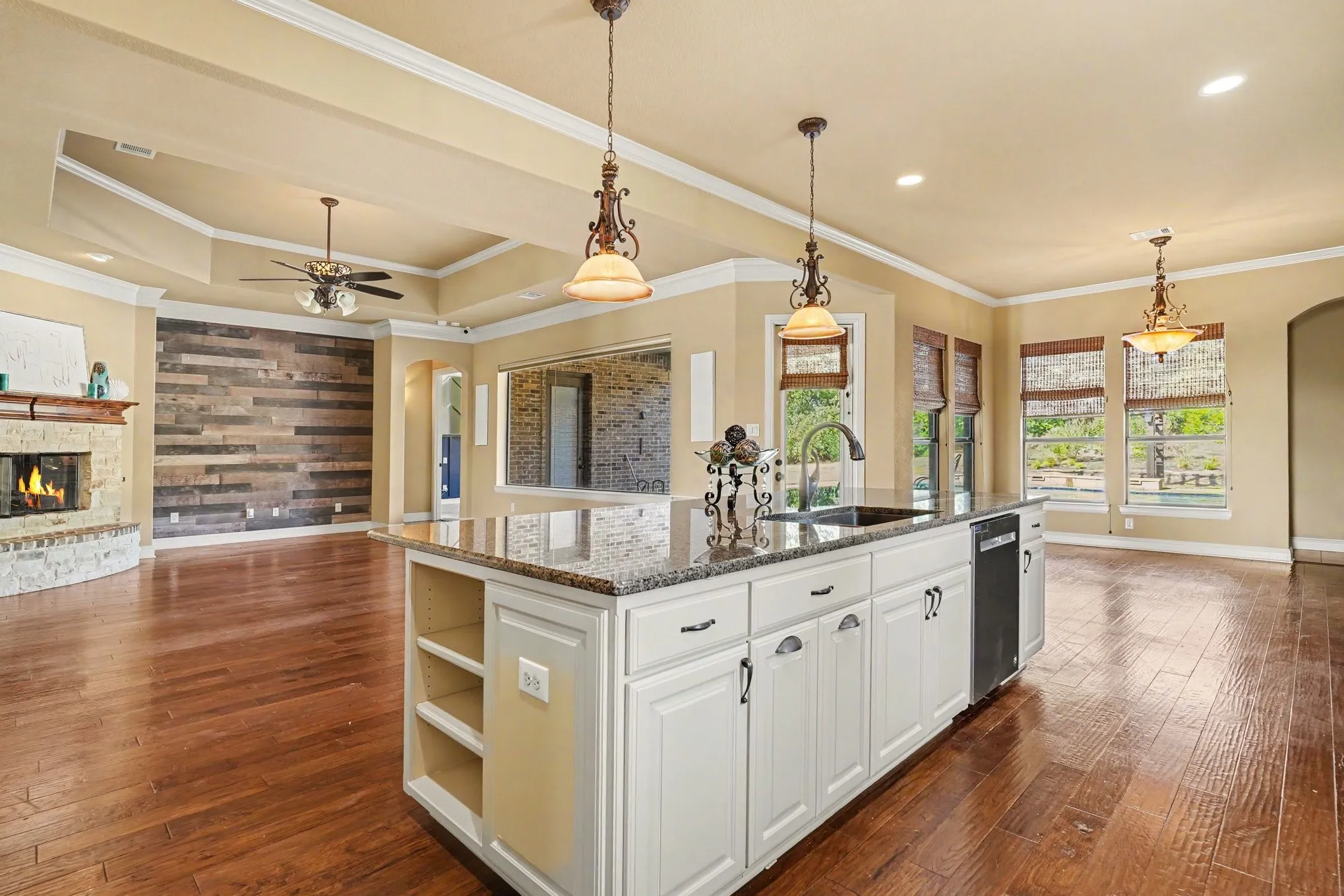 Kitchen island with white cabinetry and granite countertop, wood-finish flooring, stone-surround fireplace, wood accent wall, and tray ceiling