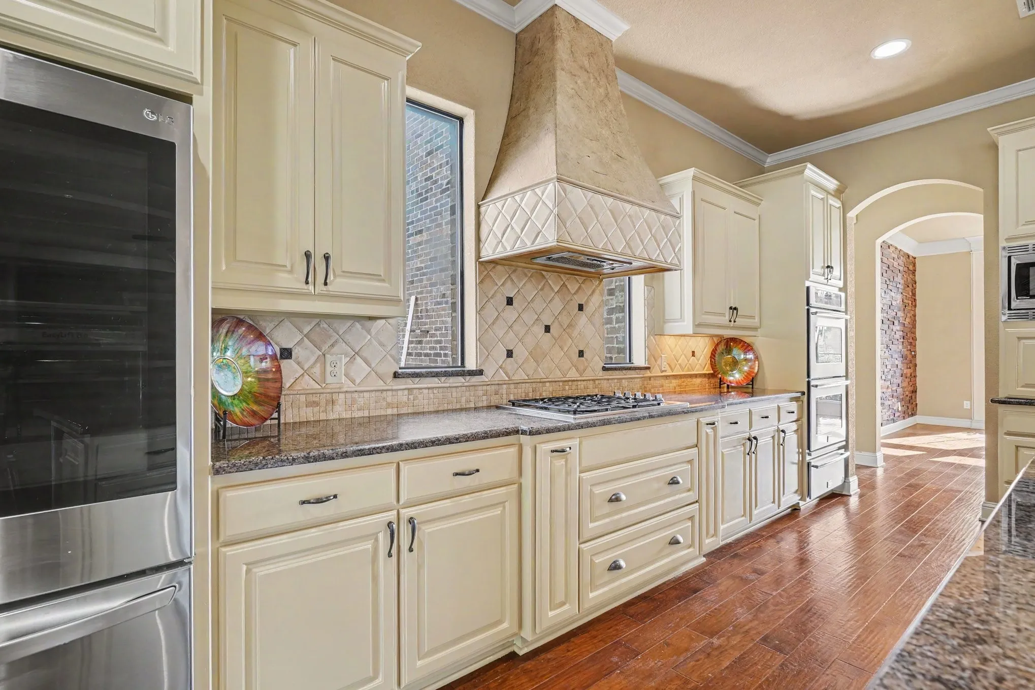Cream-finish cabinetry, granite countertops, tile backsplash, built-in stainless steel appliances, and wood-finish flooring