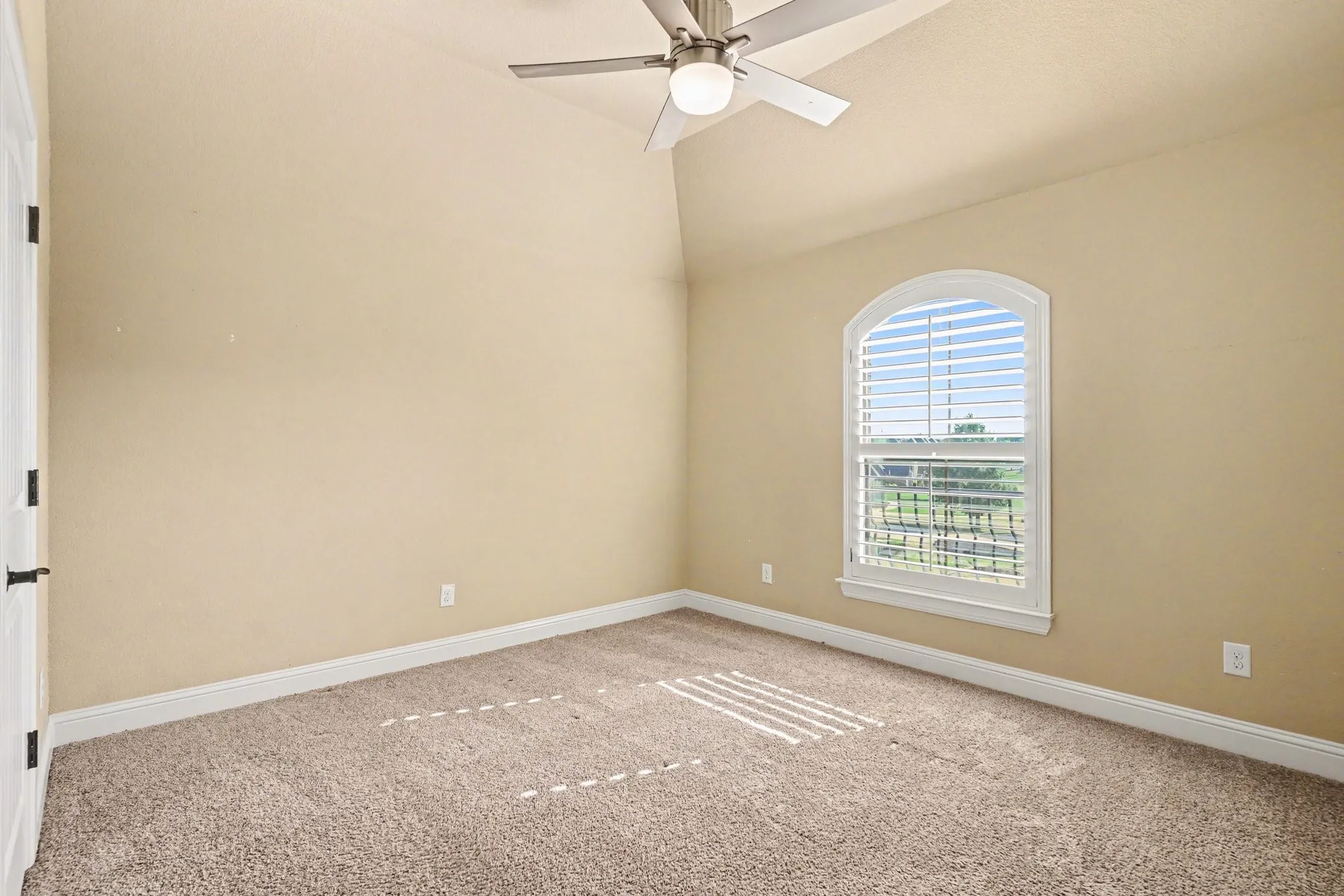 Arched window with plantation shutters, vaulted ceiling, and ceiling fan with integrated lighting with walk in closet