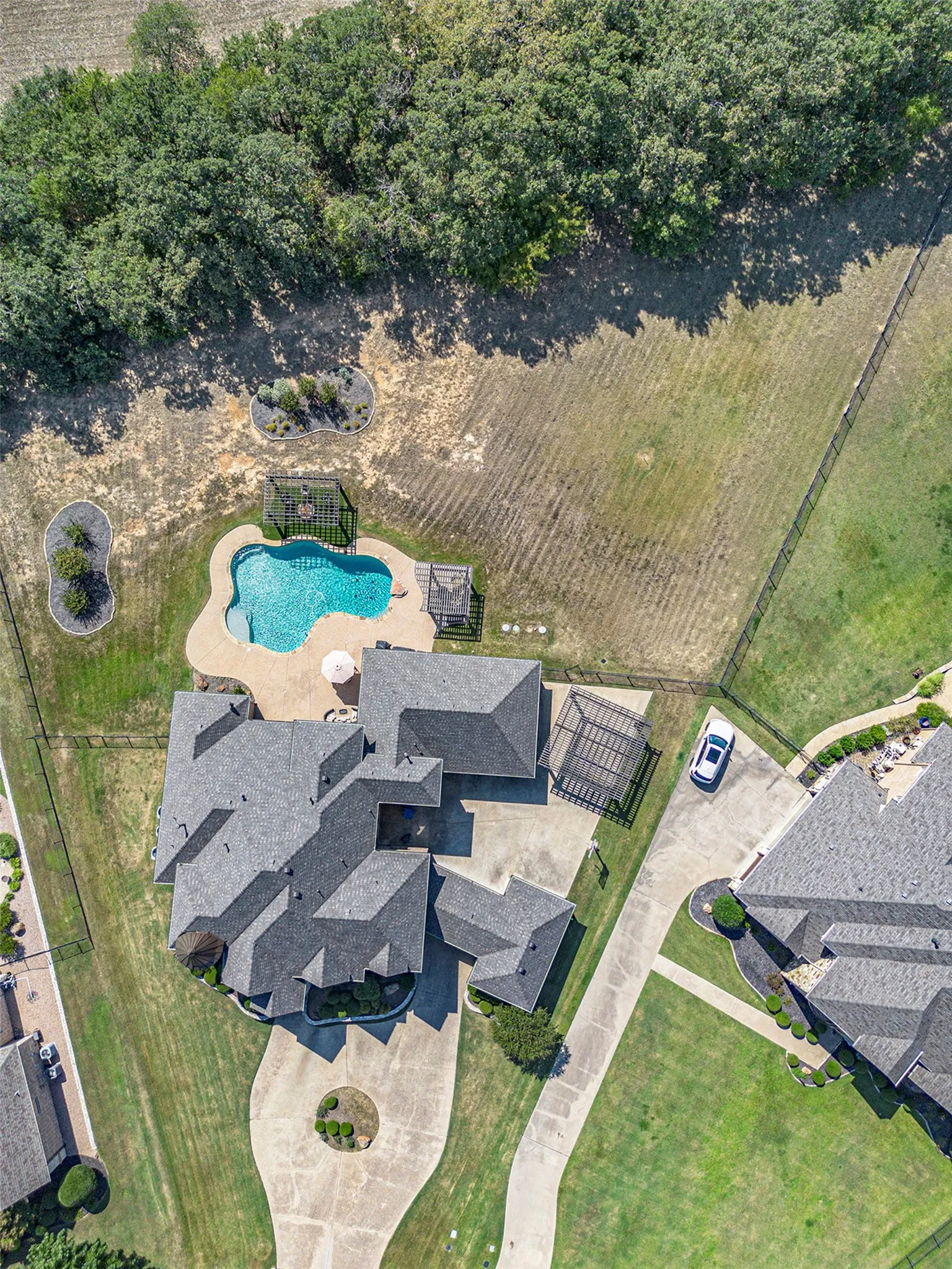 Extensive concrete driveway, multi-level shingle roof, free-form swimming pool, and a dedicated patio area