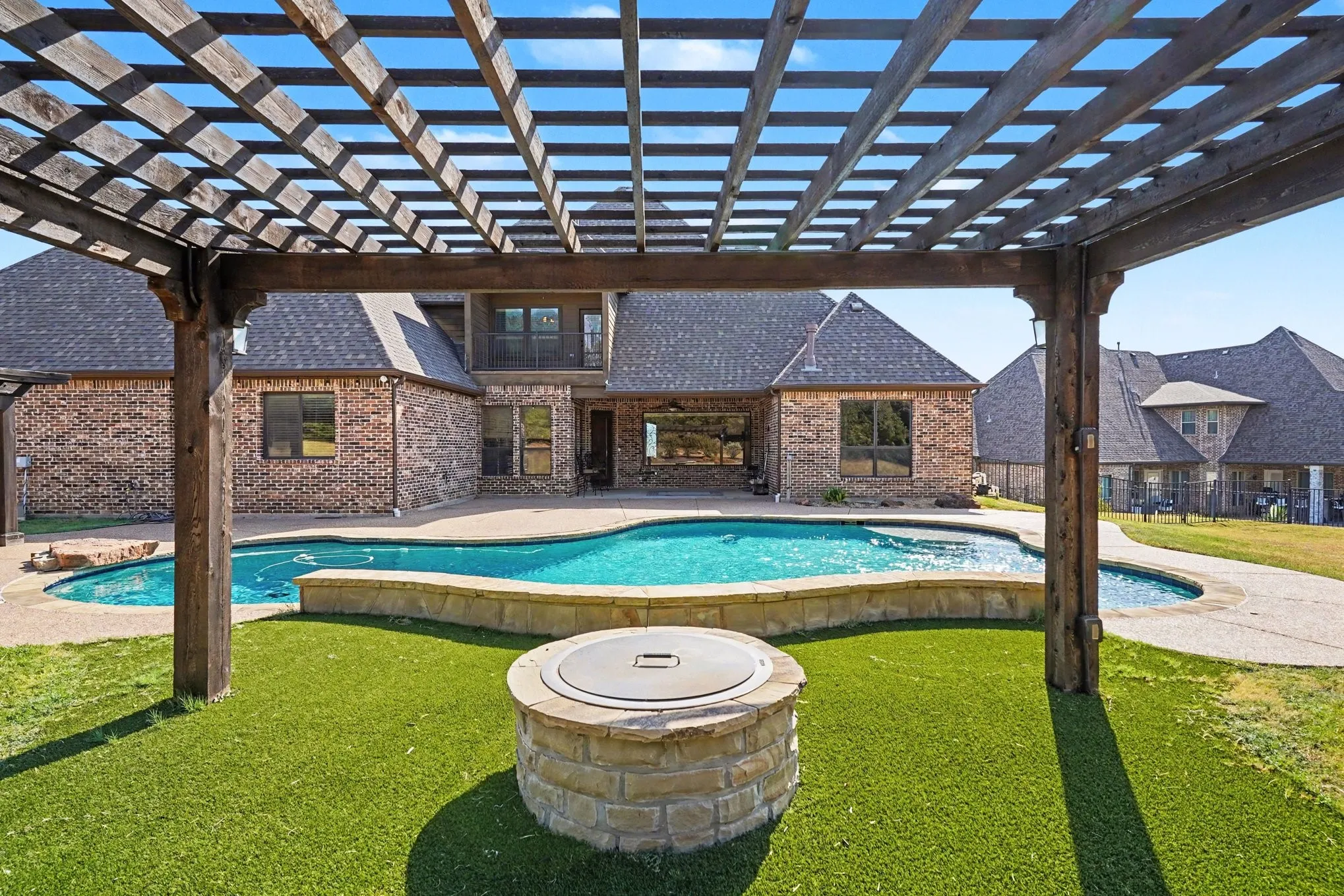 Backyard featuring a wooden pergola, freeform swimming pool, stone-clad fire pit, and artificial turf
