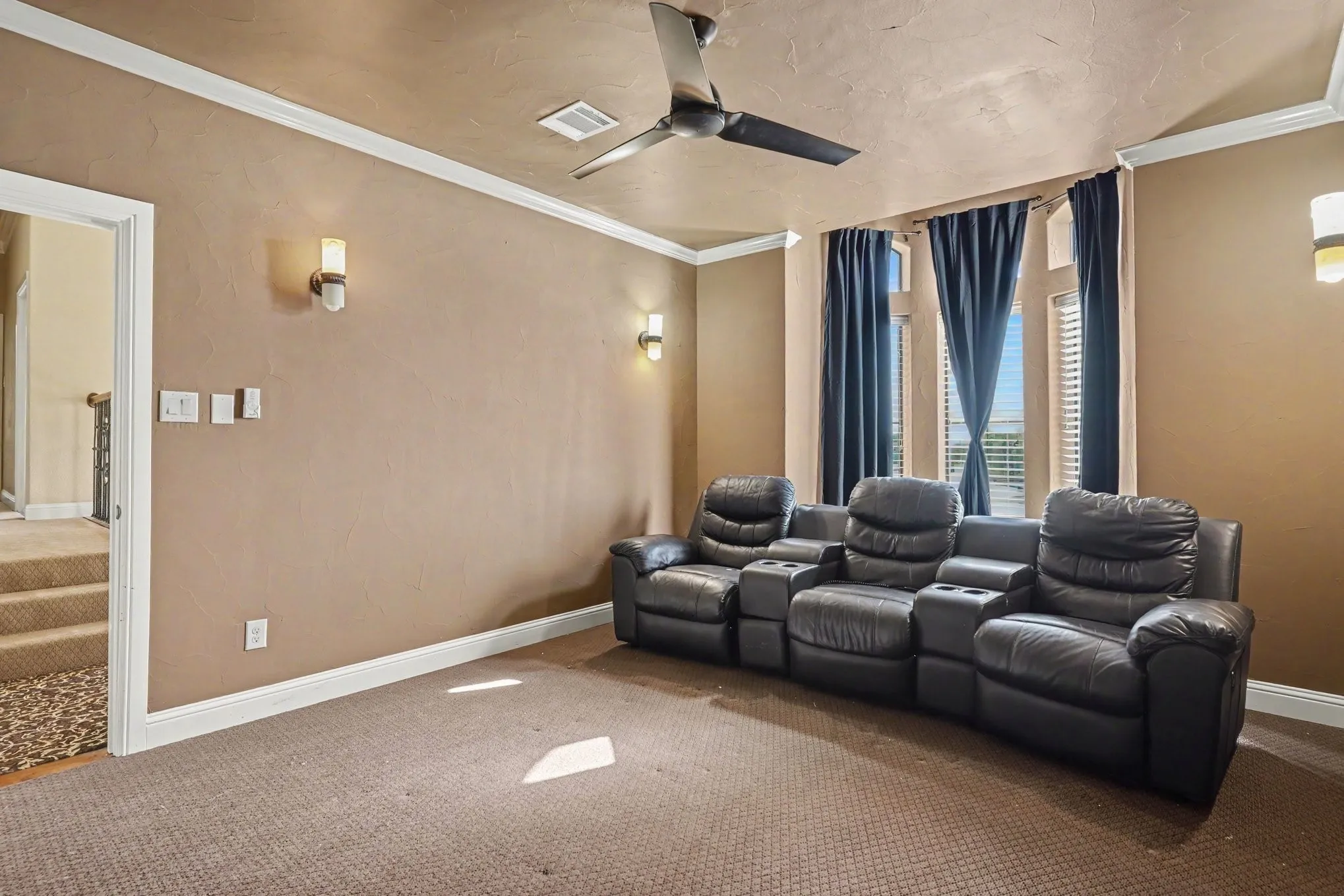 Carpeted room with crown molding, wall-mounted sconces, and a ceiling fan