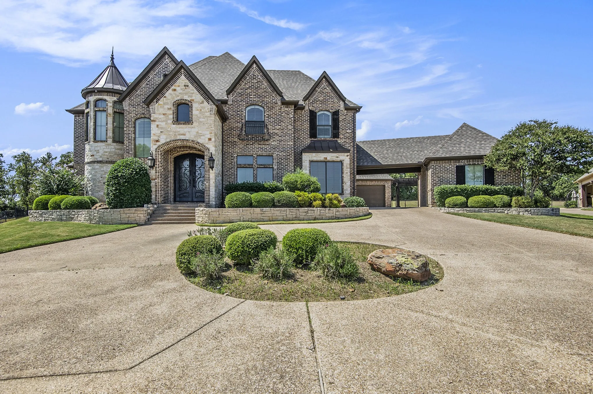 Brick and stone exterior with a turret, arched entry, decorative double doors, and a covered porte-cochère