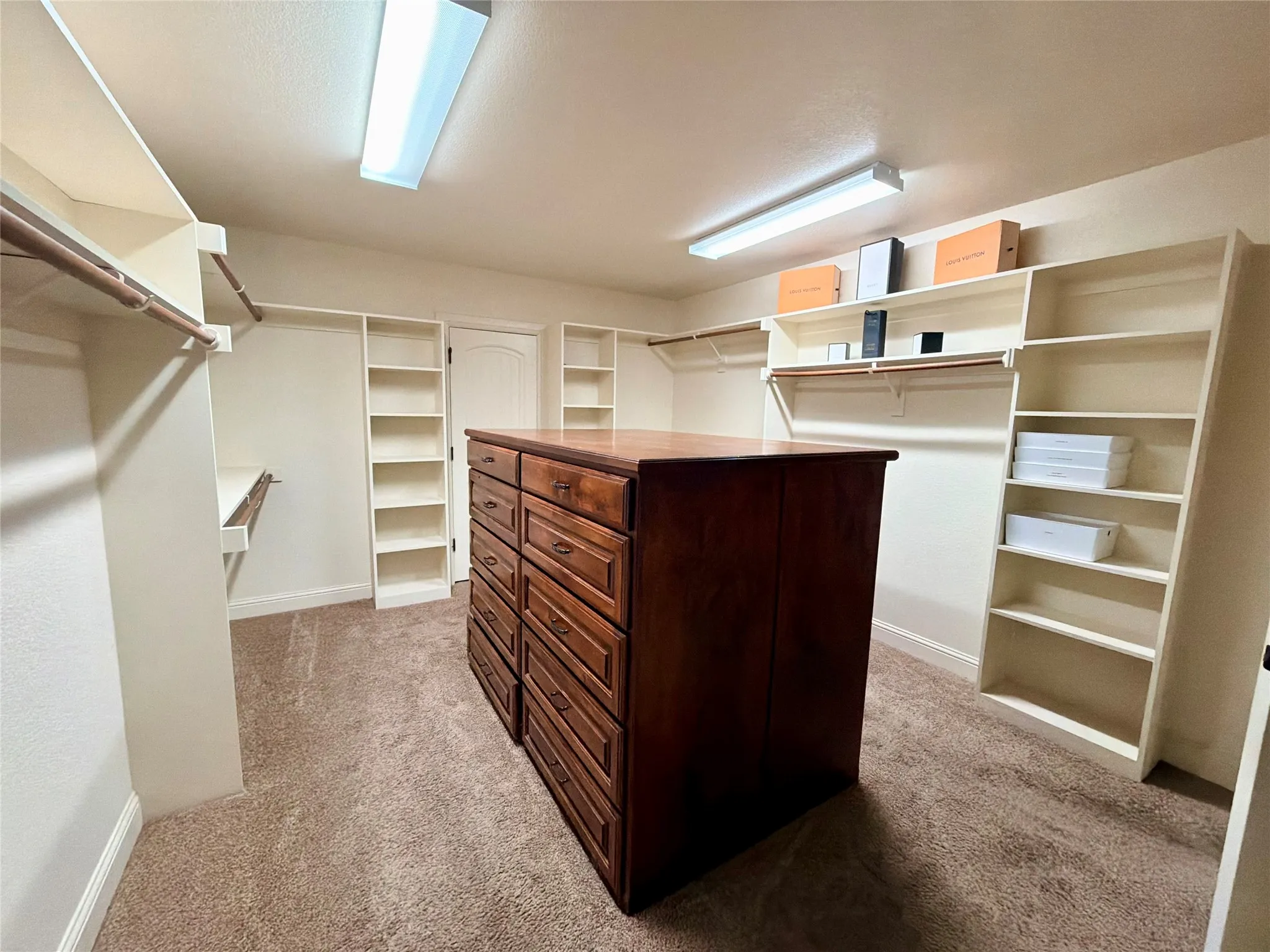 Walk-in closet featuring a central wood-finish island with multiple drawers, extensive built-in shelving, and hanging rods