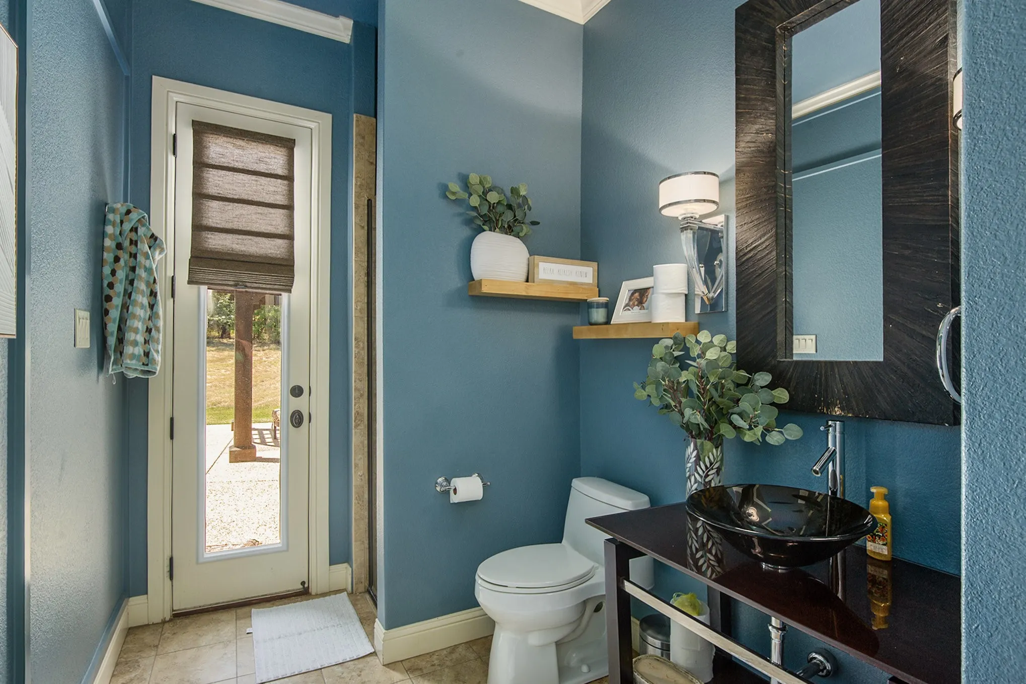 Guest bathroom with access to backyard pool area- Pedestal sink with dark finish, wall-mounted faucet, and rectangular mirror