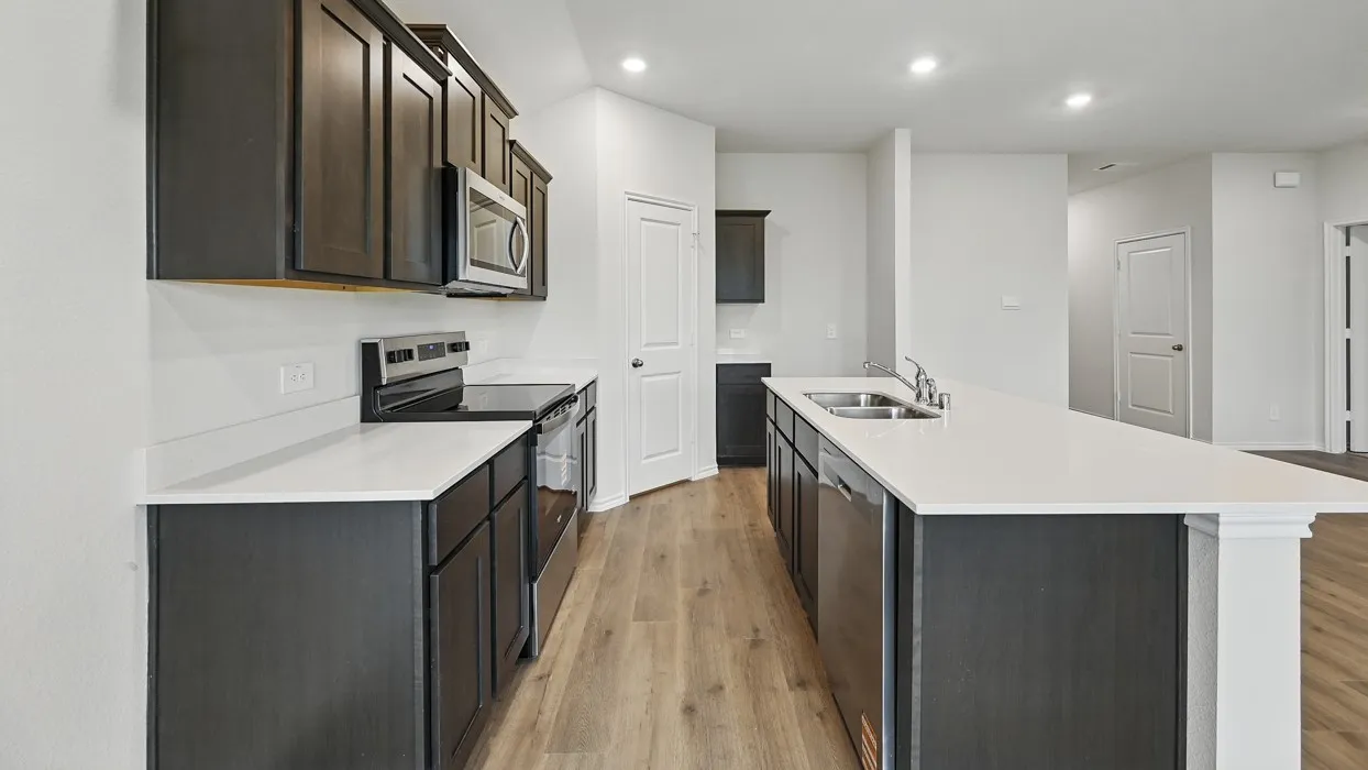 Spacious kitchen featuring dark wood cabinetry, light countertops, stainless steel appliances, a large island with an integrated sink, and wood-finish flooring