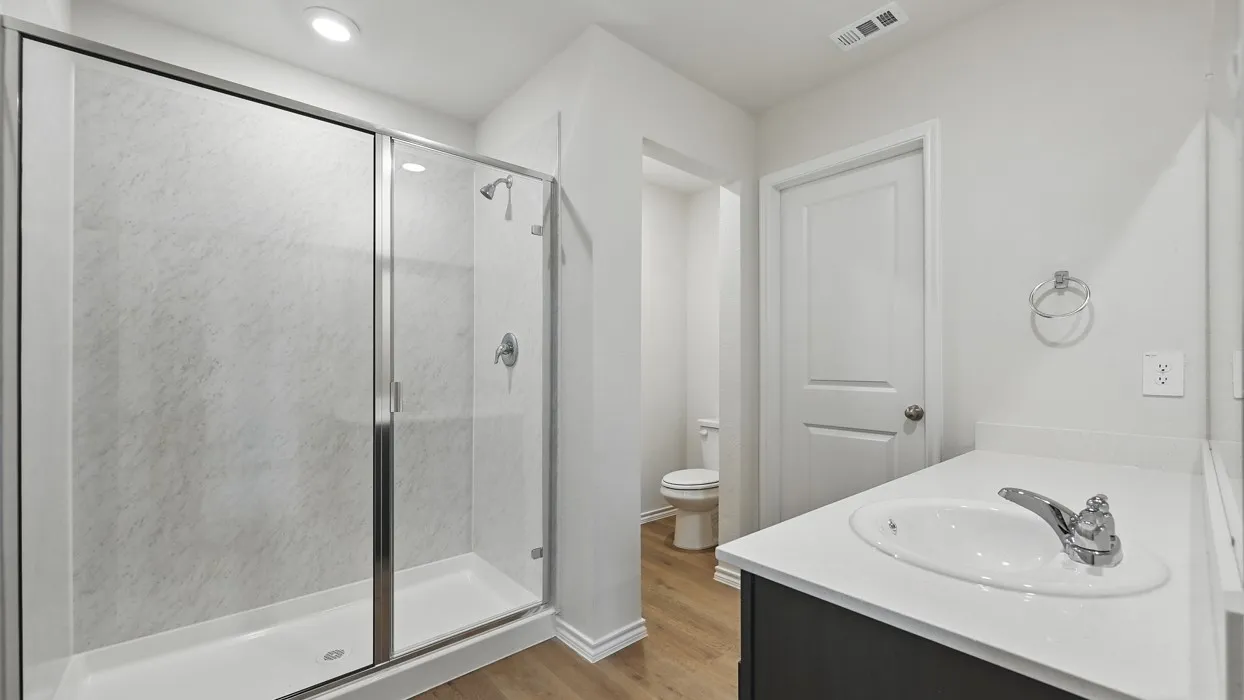 Shower with glass enclosure, single vanity with white countertop, and wood-finish flooring