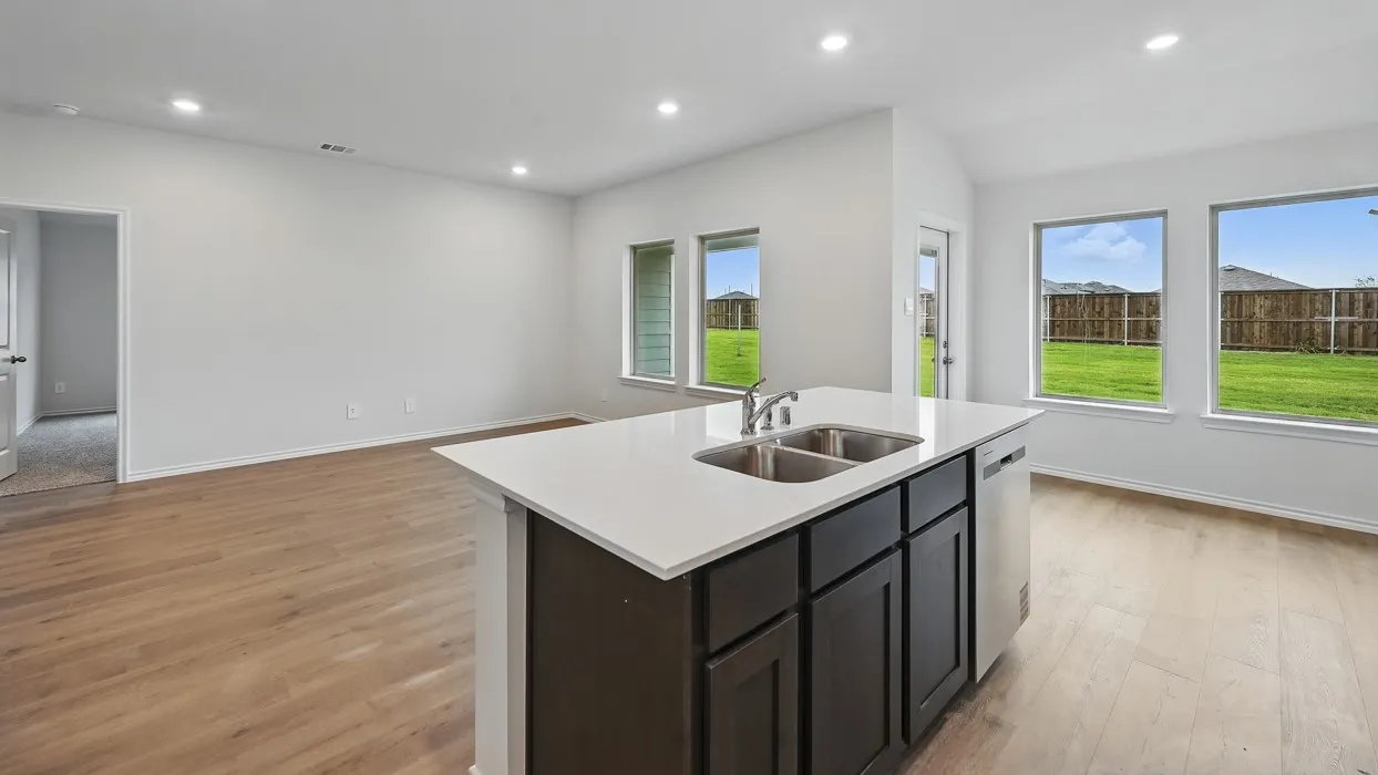 Open-concept living space featuring wood-finish flooring, recessed lighting, a kitchen island with a double basin sink, and large windows with backyard views