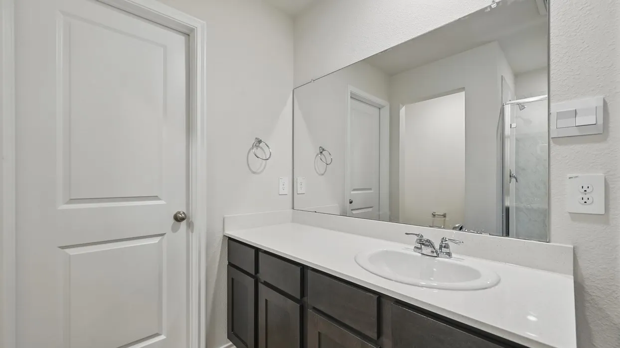 Bathroom featuring a single vanity with dark wood-finish cabinetry, a white countertop, an undermount sink with a chrome faucet, and a large wall-mounted mirror