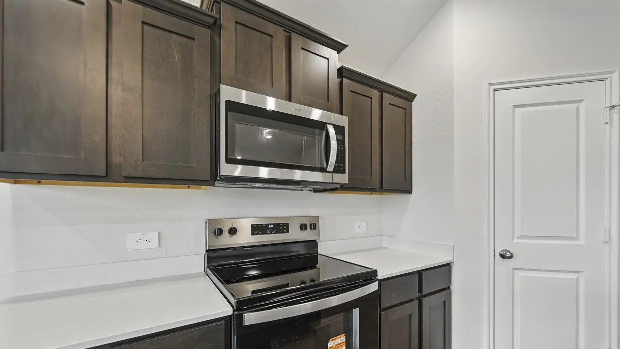 Stainless steel microwave, stainless steel electric range, dark wood-finish cabinetry, white countertops, and white door