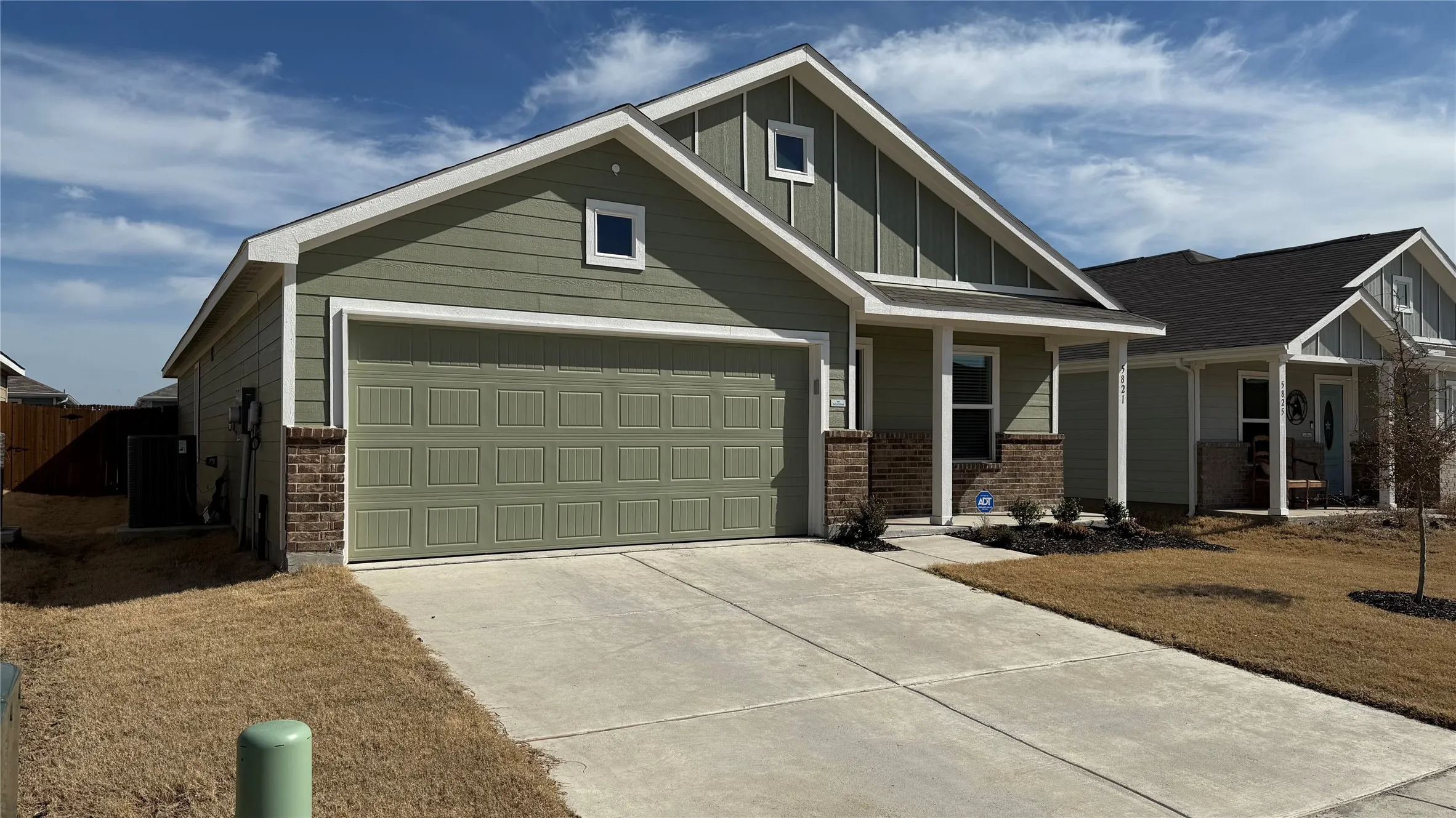 Single-story residence featuring green horizontal siding, brown brick accents, a two-car garage, and a concrete driveway