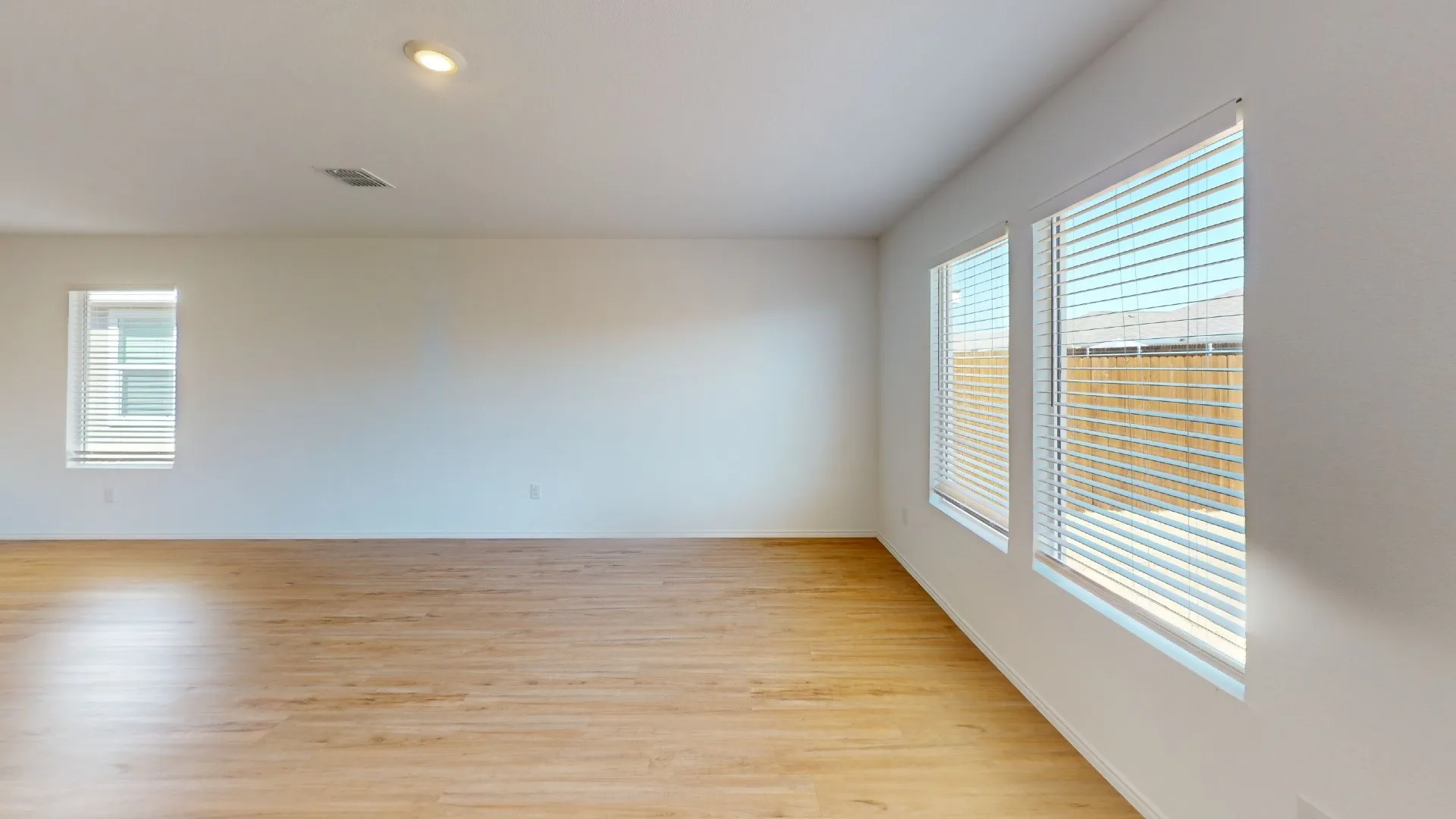 Expansive room featuring wood-finish flooring, recessed lighting, and multiple windows with blinds