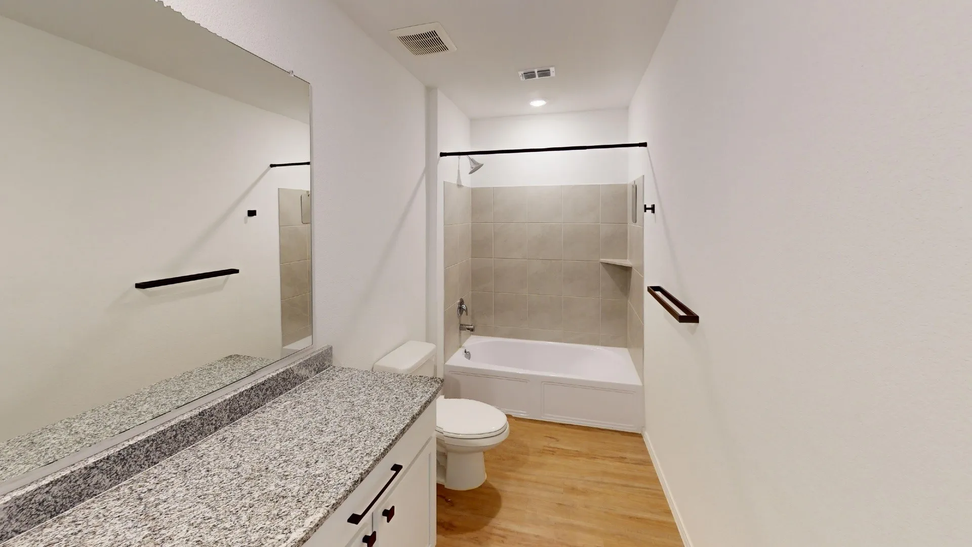 Bathroom featuring a vanity with a speckled countertop, a toilet, a bathtub with a tiled surround, and wood-finish flooring