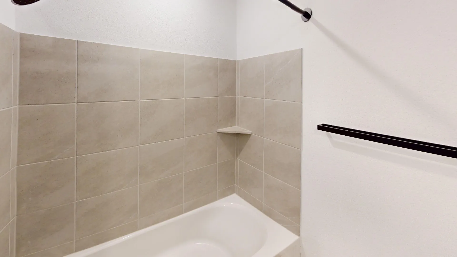Bathtub with neutral-toned tiled surround, integrated corner shelf, and matte black shower fixtures