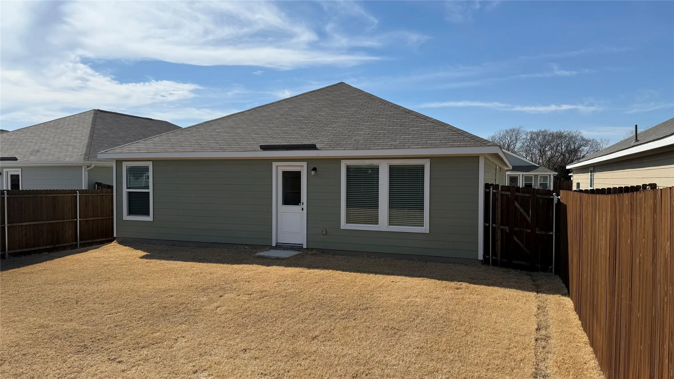 Private fenced backyard featuring a side entry gate, exterior entry door, and multiple windows