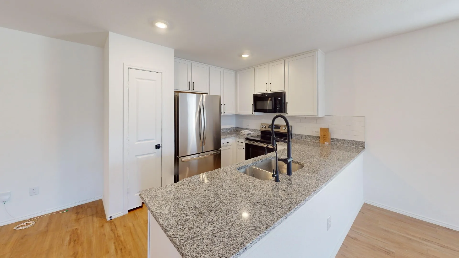 Kitchen featuring light wood-finish flooring, white cabinetry, stainless steel appliances, speckled stone countertops, and a black faucet