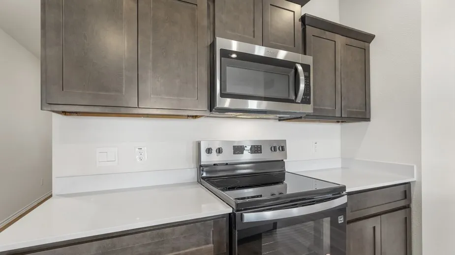 Gray shaker-style cabinetry with crown molding, stainless steel microwave, electric range, and light-toned countertops
