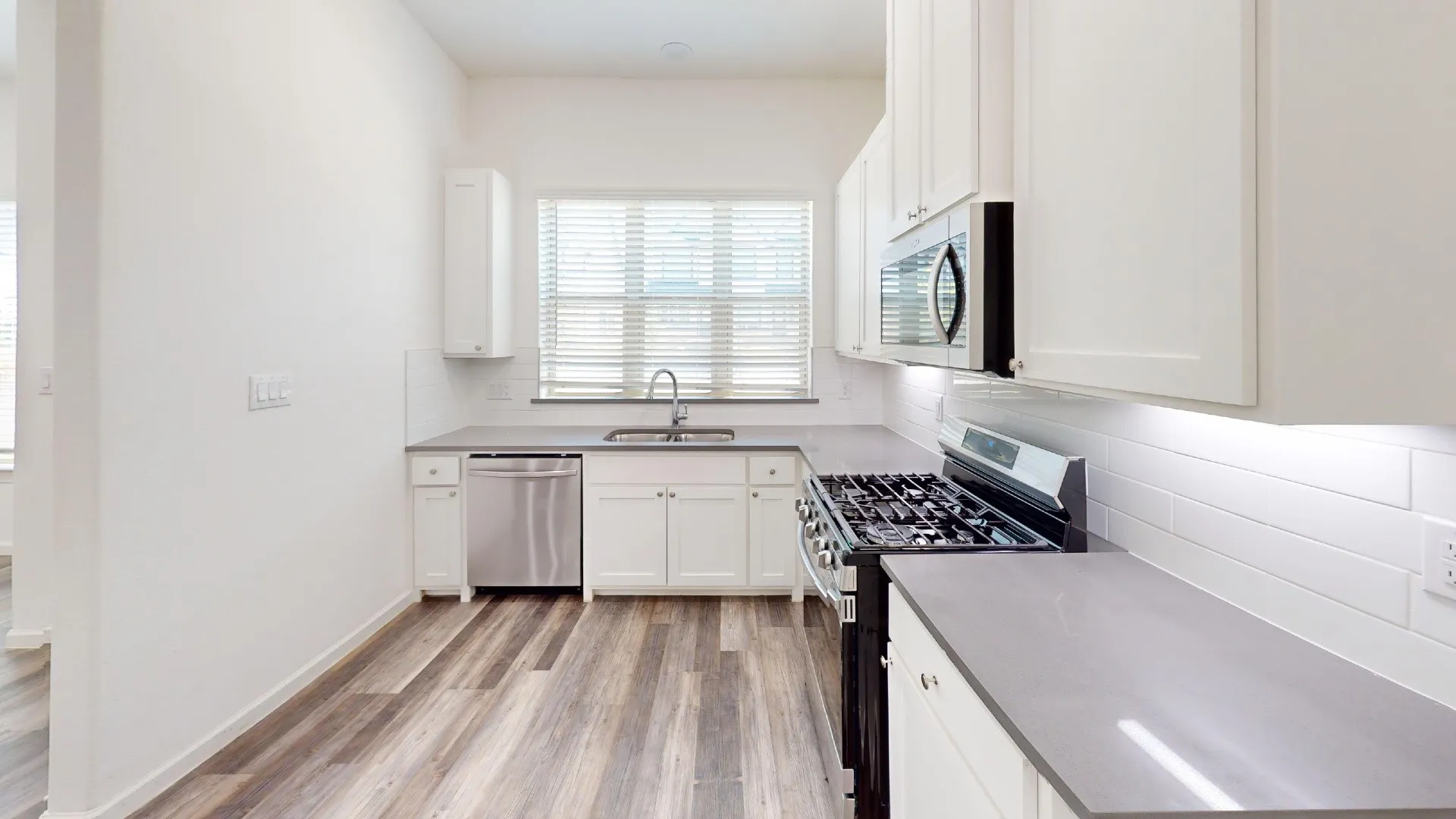 Kitchen featuring wood-finish flooring, white cabinetry, sleek countertops, white subway tile backsplash, and stainless steel appliances