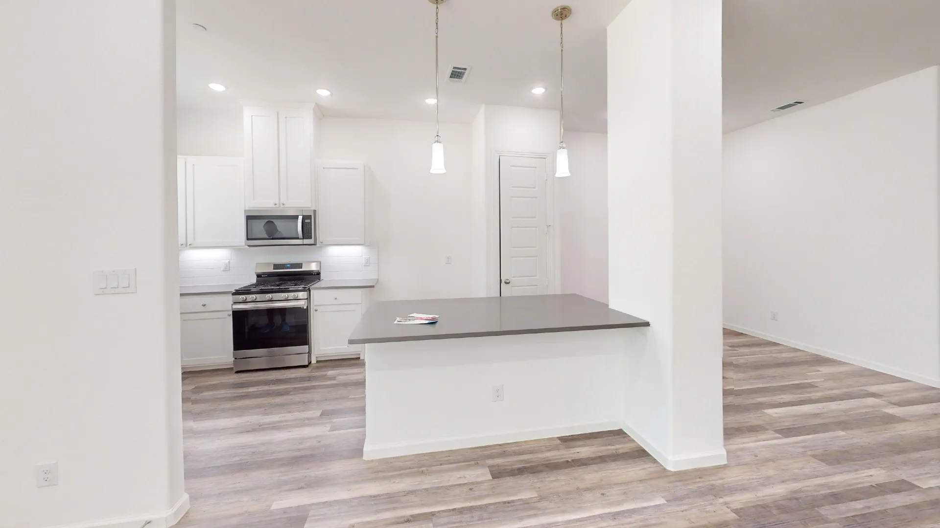 Modern kitchen featuring white cabinetry, stainless steel appliances, a dark countertop island, and wood-finish flooring