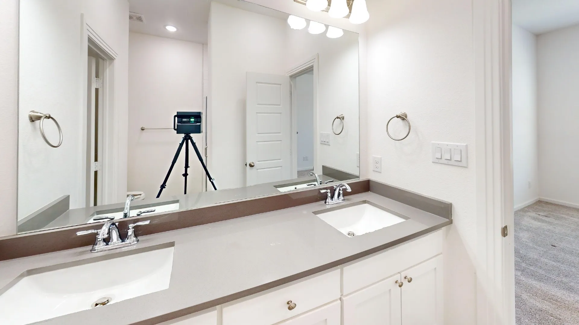 Dual undermount sinks with chrome fixtures, light gray countertop, white cabinetry with silver hardware, and wall-mounted vanity lighting