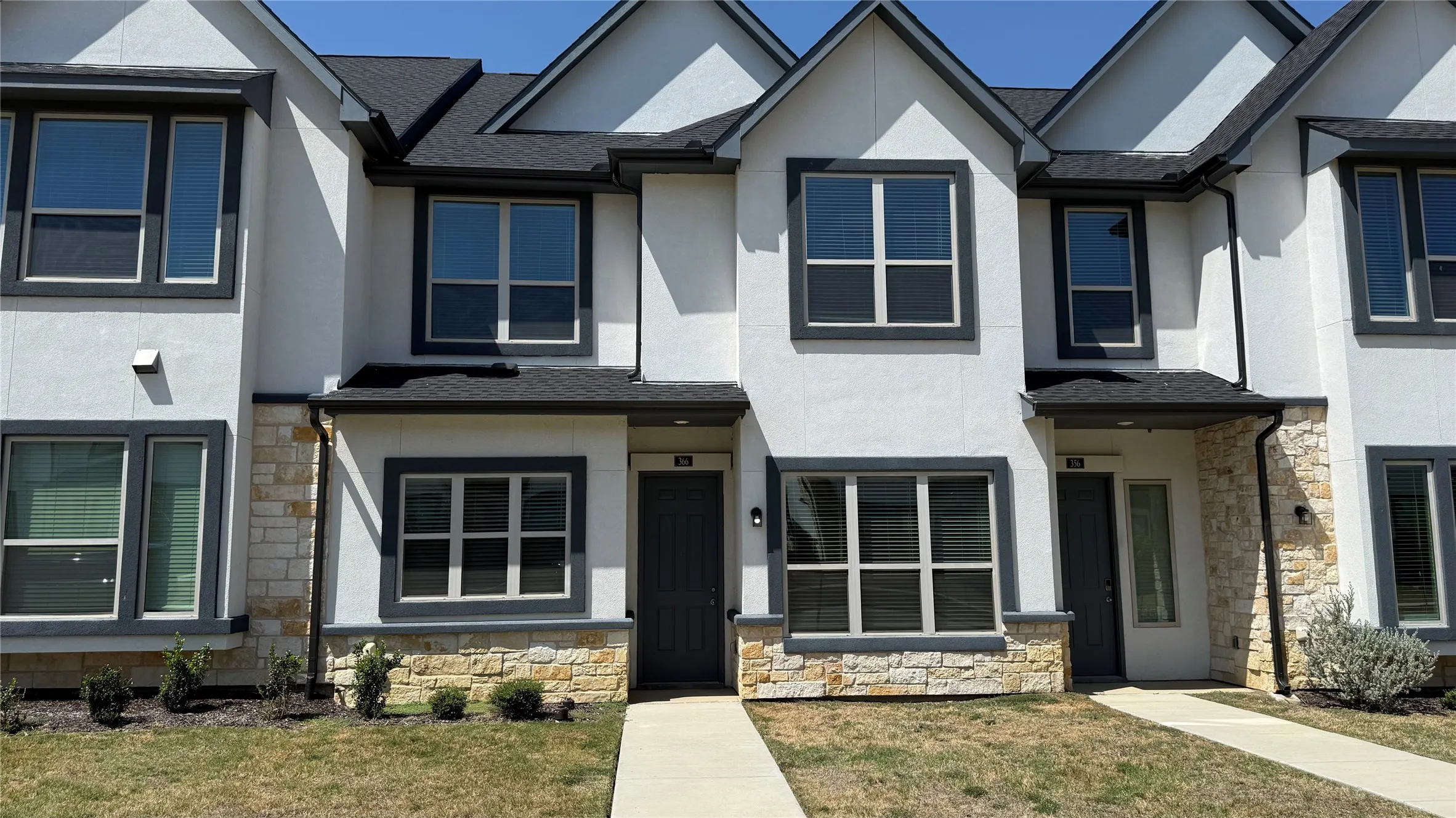 Modern townhouse exterior with white stucco siding, dark trim windows, and a prominent dark roof