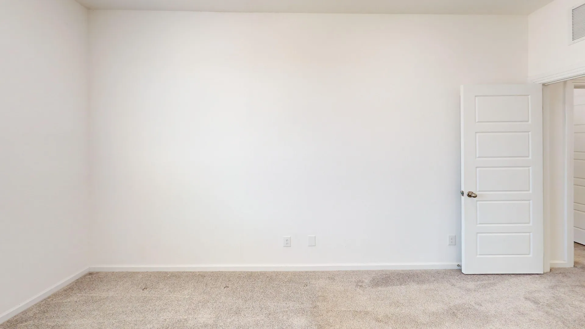 Carpeted flooring with white baseboards, a white paneled door with a metallic knob, and white painted walls