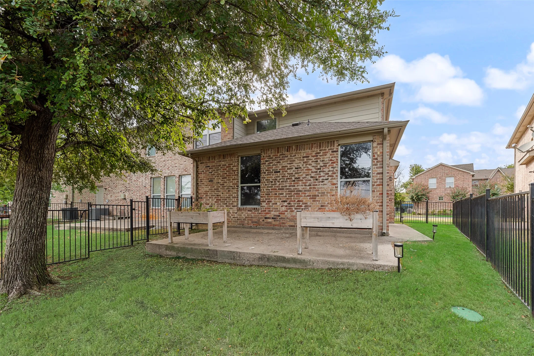 Manicured lawn with a concrete patio, brick exterior, and black metal fencing