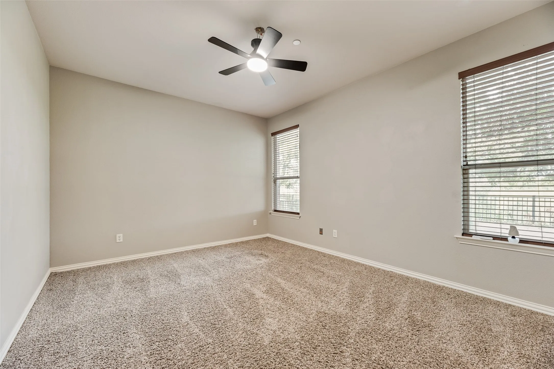 Carpeted room featuring a ceiling fan with integrated lighting, two windows with blinds, and neutral wall tones