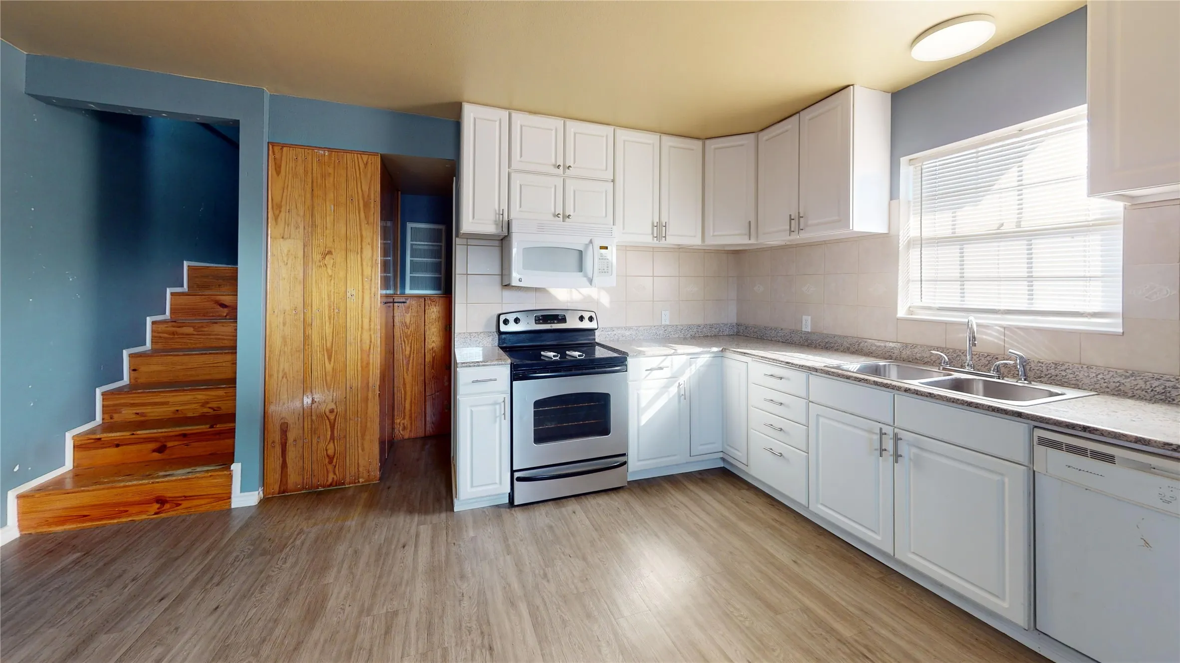 Kitchen featuring white cabinetry, stainless steel appliances, a double basin sink, and wood-finish flooring