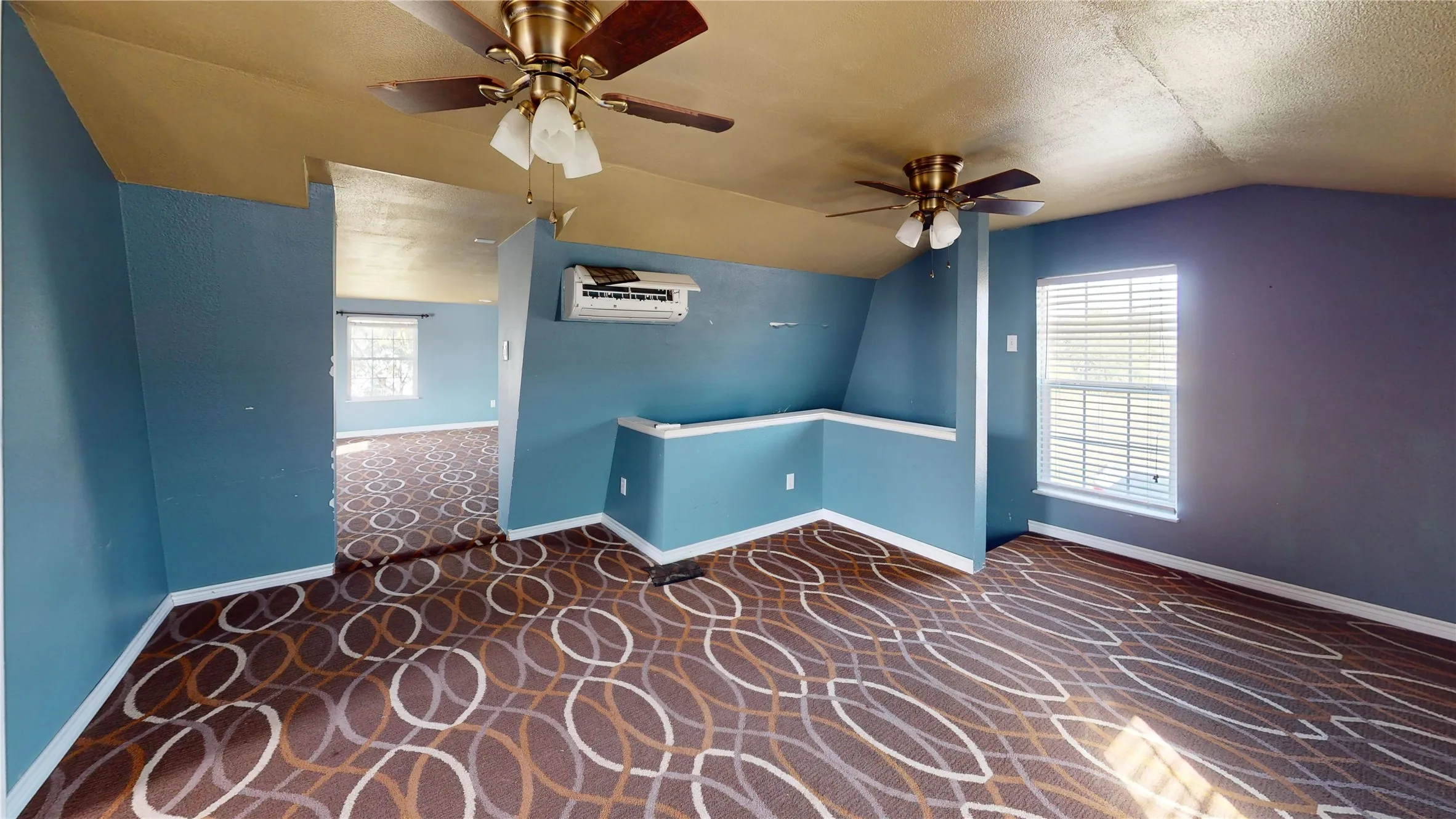Patterned carpeting, two ceiling fans, and a wall-mounted air conditioning unit
